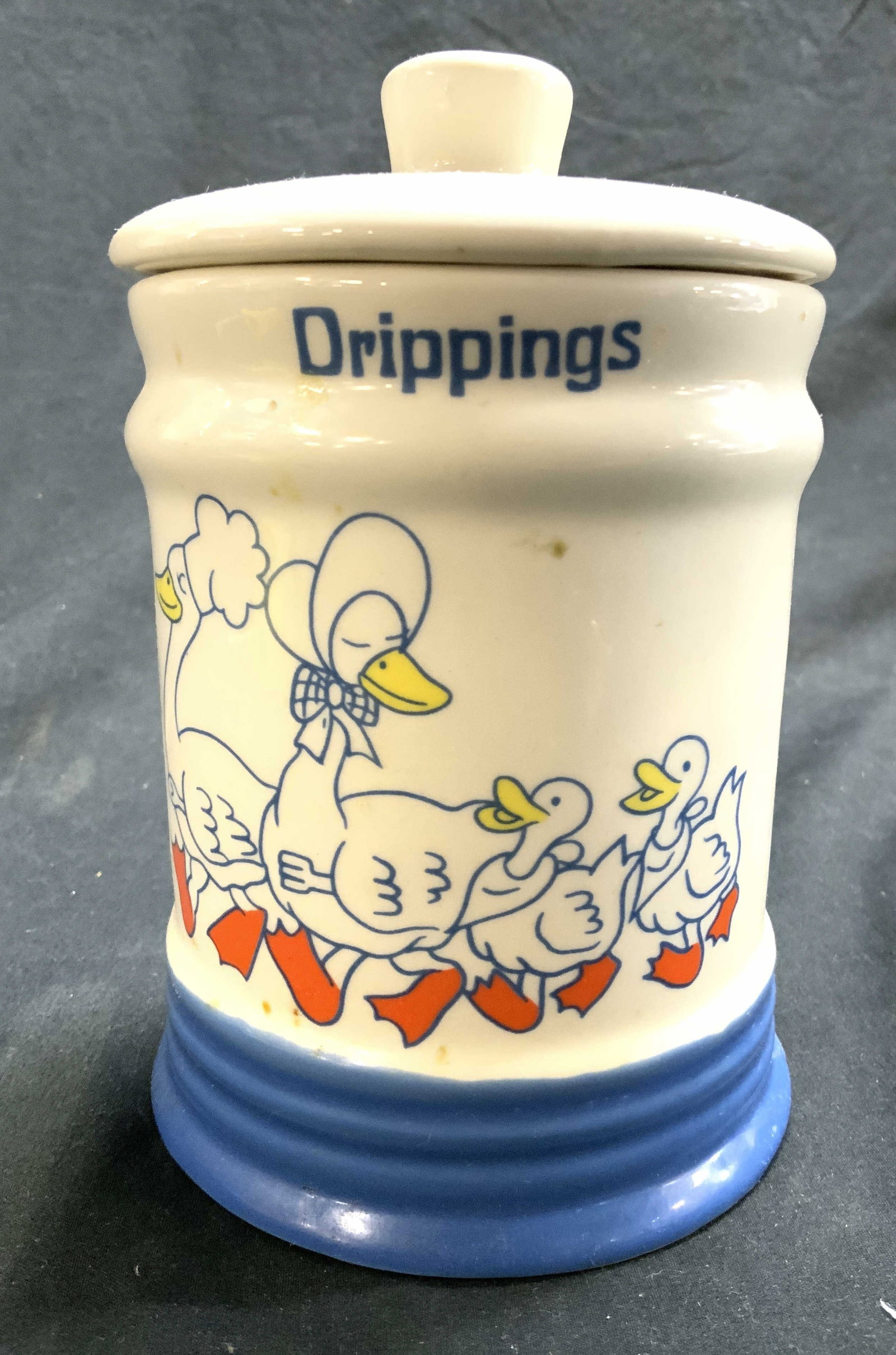 Vtg Duck Detailed Porcelain DRIPPINGS Jar W Lid: Jar is vintage and porcelain. Piece includes lid. Jar has detail depicting family of 4 Ducks. Jar reads DRIPPINGS. Piece is cream with blue toned base. Jar measures approximately 6 inches tall 4 inche