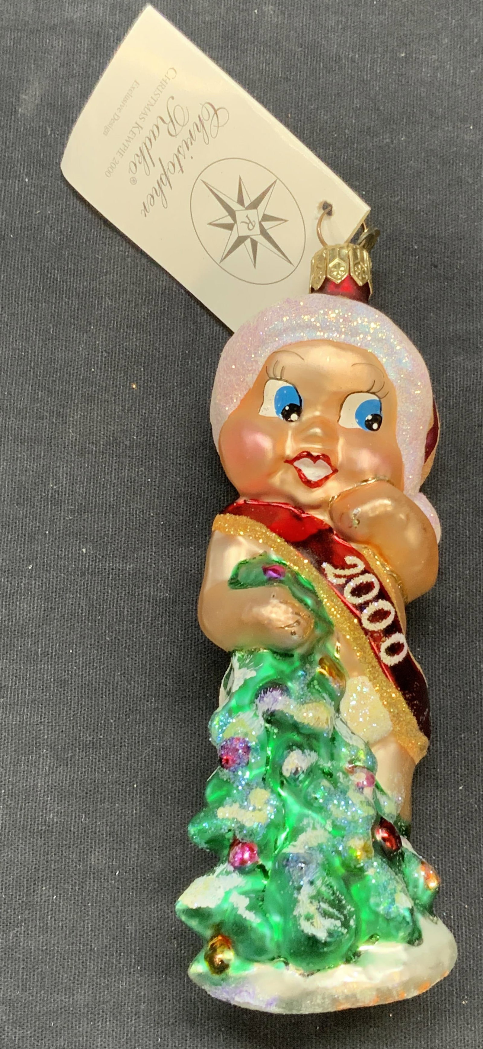 Christopher RADKO Glass Baby Ornament, 2000: Christopher RADKO Christmas Kewpie glass baby motif ornament. Produced 2000. Measures approx. 5 inches long. Includes original box. Some surface wear including scratching observed. Christopher RADKO, 