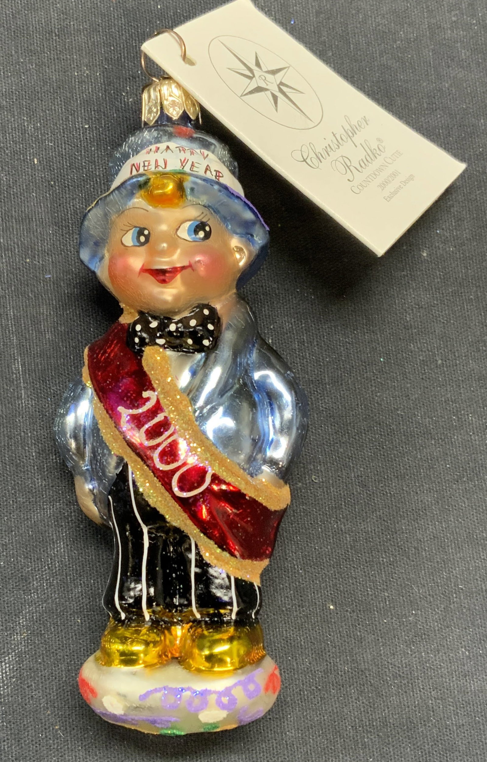 Christopher RADKO New Years Baby Ornament, 2000: Christopher RADKO Countdown Cutie glass baby motif ornament. Produced 2000/2001. Measures approx. 4.5 inches long. Includes original box. Some surface wear including scratching observed. Christopher R
