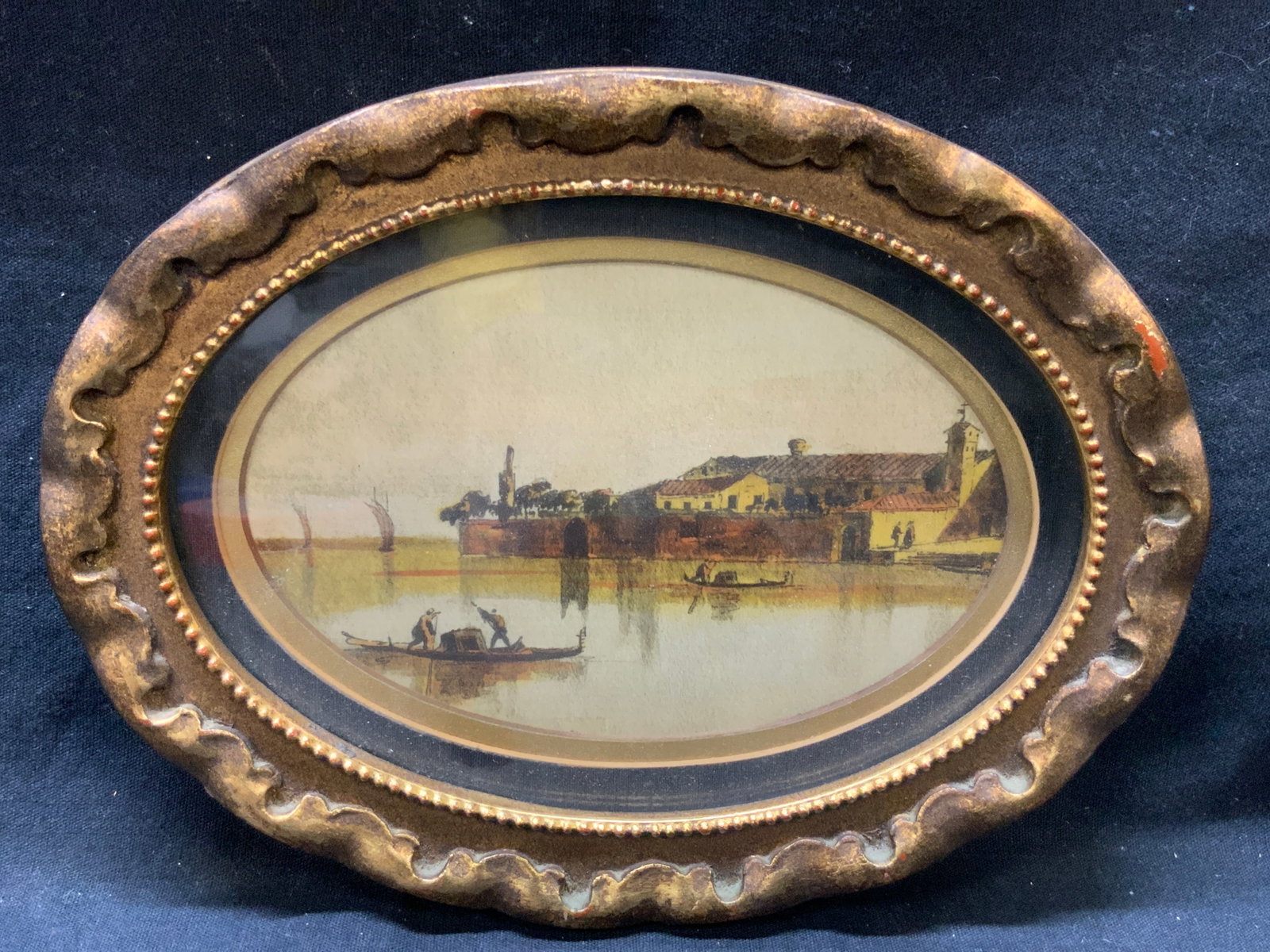 After Canaletto Landscape Colored Lithograph: After Canaletto, colored litho depicting a landscape of a homestead against a body of water with people in boats on the water. Framed in a gold leafed wooden frame. Approx 6 x 8 inches window measures