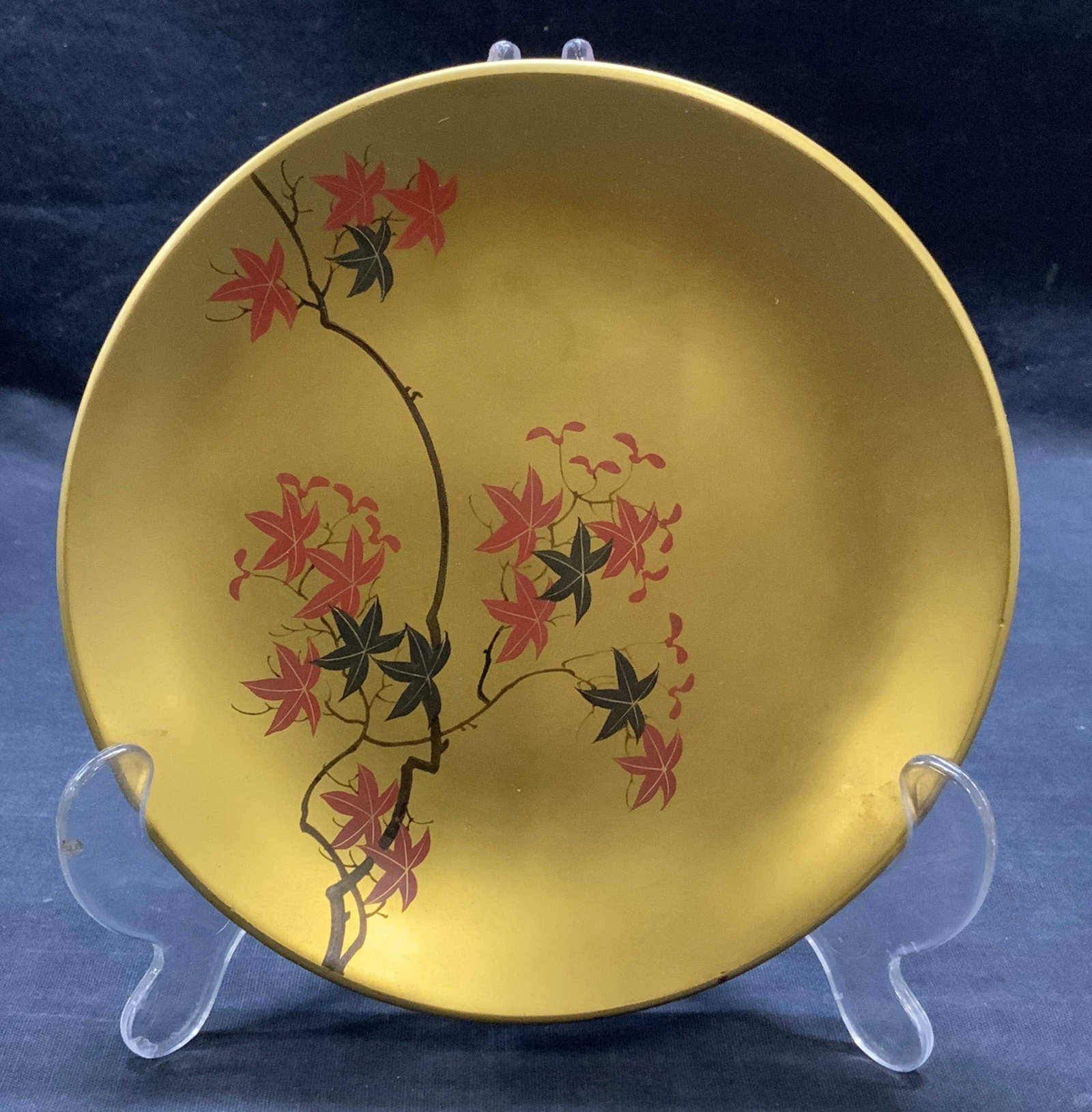 Gilt Lacquered Botanical Tree Plate: Lacquered plate with botanical maple tree motif. Gilt with hues of black and red. Measures approx. 6.75 inches diameter. Composite material. Some surface wear Including scratching observed. Lacquered 
