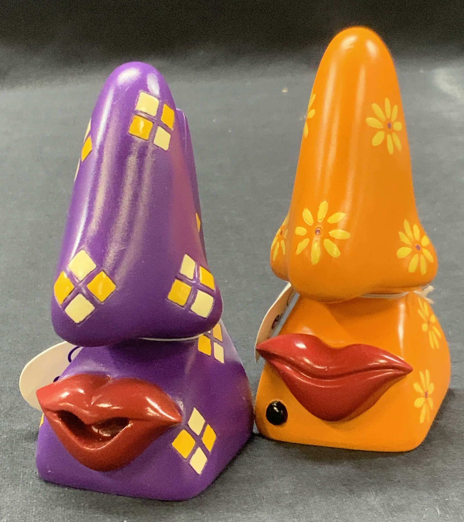 Lot 2 Hard Composite Nose Eye Glass Holders: Lot of 2 Hard composite made eye glass holder in the shape of a nose with a pair of red lips, one purple and orange with diamond and flower patterns. Approx 4 inches tall. Minor wearing to base of hol