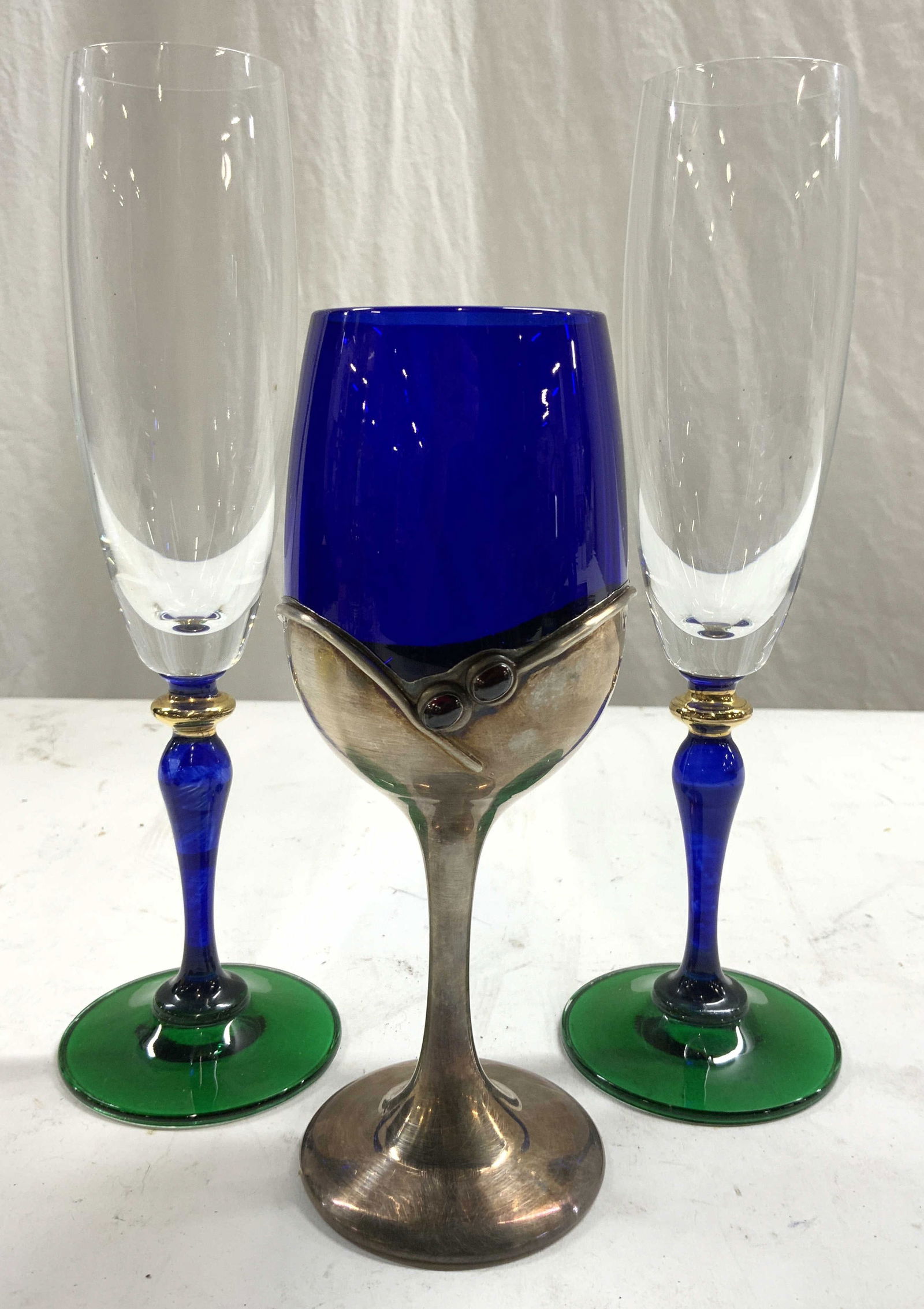 Sterling Silver DONAR Israel Stem Goblet & Flutes: Underside of goblet is inscribed 925 DONAR ISRAEL. Lot includes 1 art glass goblet with sterling silver stem and cobalt blue basin. Lot also includes 2 glass champagne flutes each with gilt, blue and