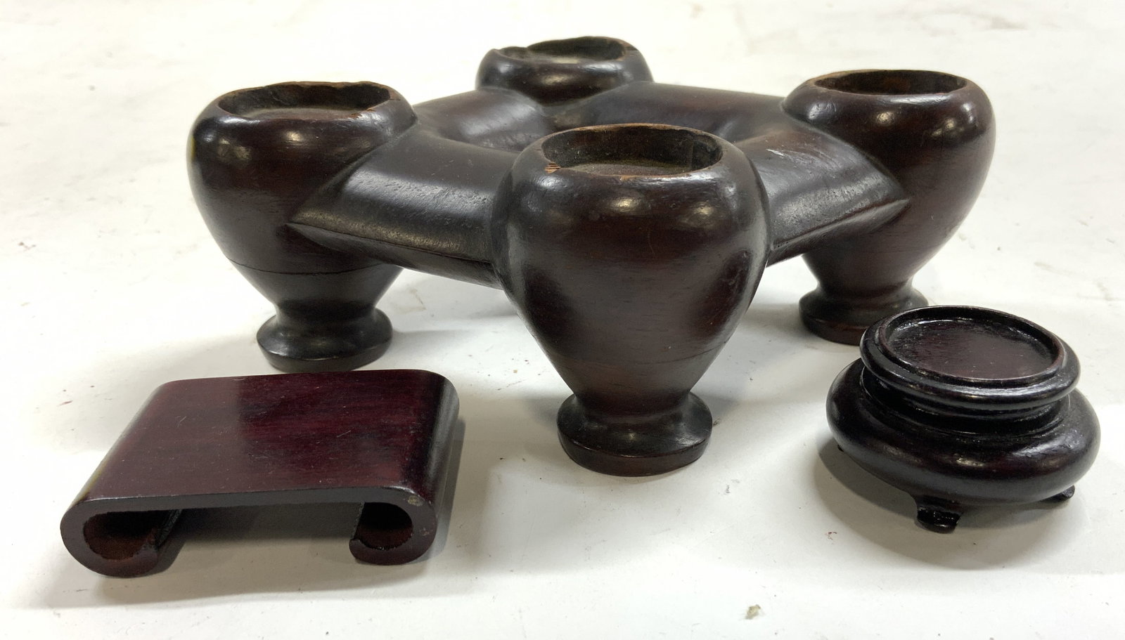 Lot 3 Carved Wooden Stands Pedestals: Lot includes 3 pedestals, includes 1 circular shaped pedestal 1 pedestal with area for 4 objects, & 1 pedestal with scrolled edges. Each are brown toned and wooden. Largest piece measures approximatel