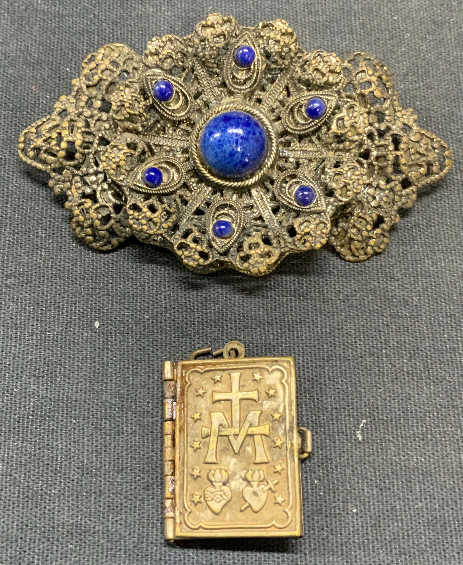Lot 2 Vintage Silver Tn Brooch & Book Locket: Vintage silver tone filigree blue cabochon brooch and silver tone book locket pendant. Brooch measures approx. 2.75 x 1.5 inches. Locket measures approx. 1 x .75 inches. Both pieces have surface wear