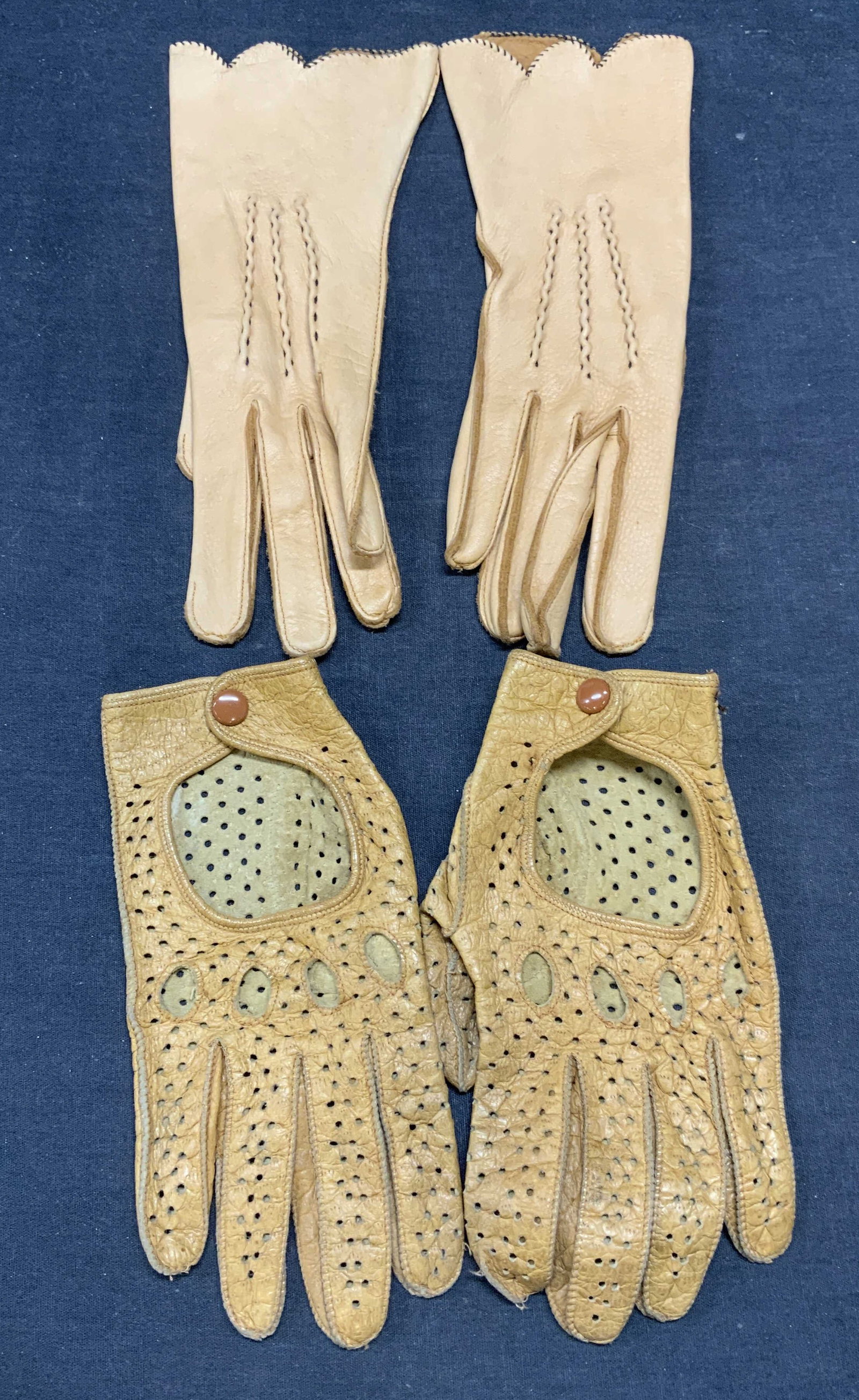 Lot 2 Tan Leather Gloves: Lot of 2 pairs of tan leather gloves. 1 pair perforated leather and 1 pair with stitched piping. Longer measure approx. 9 inches long. Both pairs have some wear to leather consistent with exposure. La
