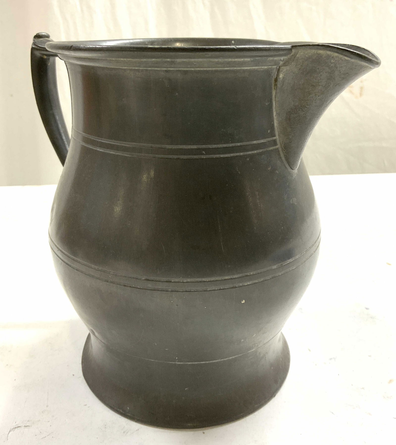 Vintage Silver Toned Pewter Pitcher: Pitcher is vintage. Piece is silver toned and appears to be pewter. Pitcher has horizontal line relief detail. Piece measures approximately 7.5 inches tall 5.5 inches wide 8.25 inches deep. Pitcher, p