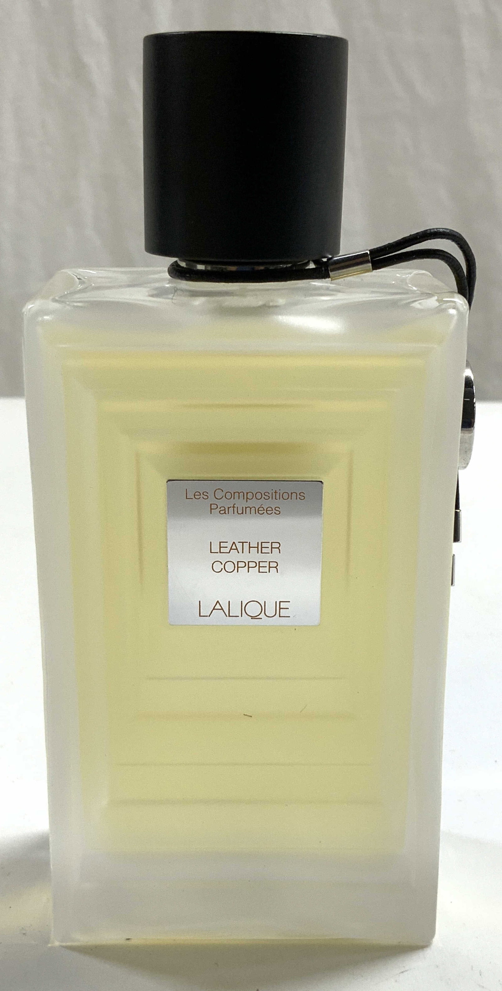 LALIQUE Leather Copper EDP Tester 3.3 Fl Oz: Bottle reads LALIQUE Leather Copper. Bottle has is frosted. Fragrance liquid in yellow toned. Piece has black and silver toned cap. Bottle is mostly full. Bottle measures approximately 5.5 inches tall