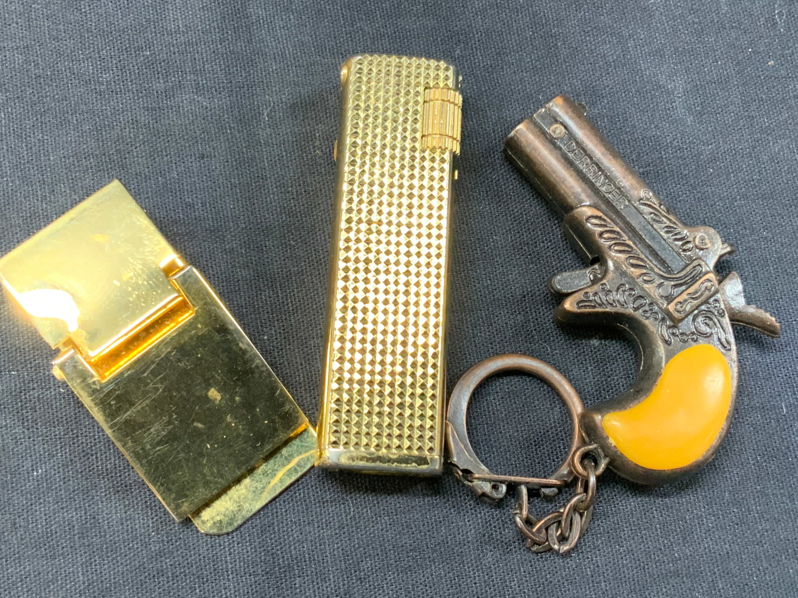 Lot 3 Brass & Metal Accessories: Lot of 3 metal accessories. 1 brass lighter marked Nesor, approx 2.5 inches tall, 1 bronze toned revolver key chain at 4 inches long and 1 brass made money clip at 2 inches long and 1.75 inches wide. 