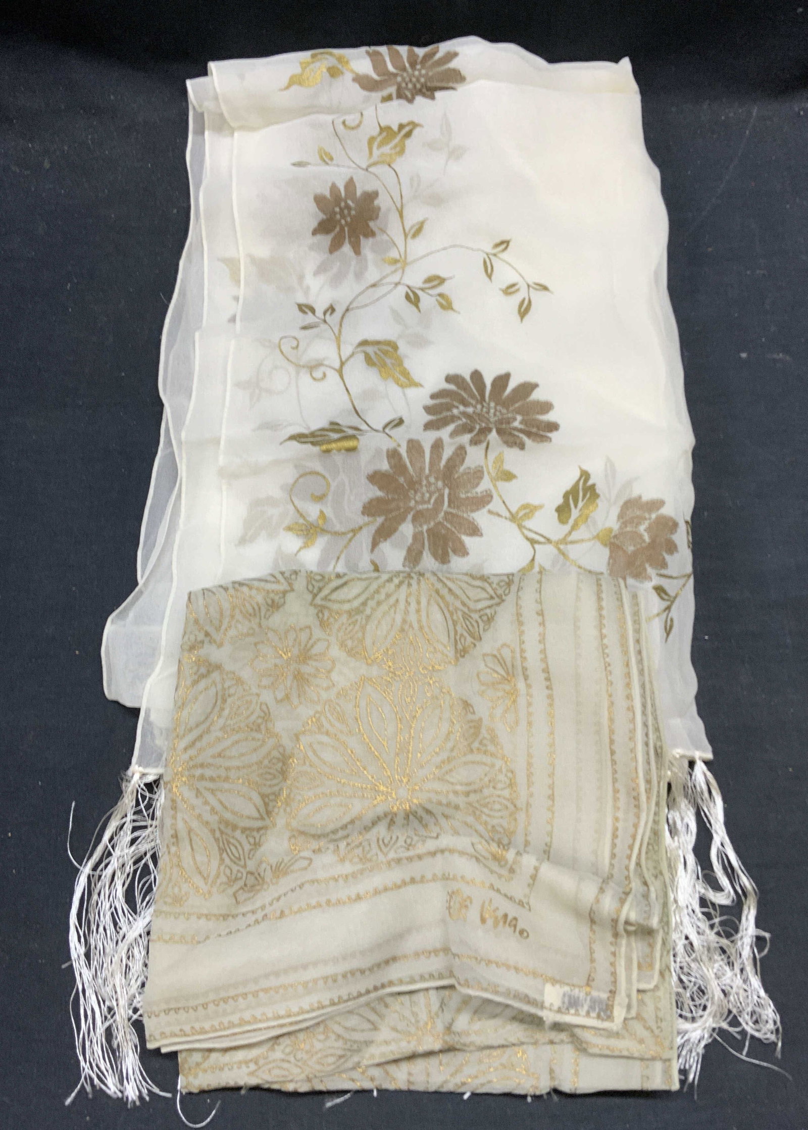 Lot 2 Vera Green Silk Floral Scarf, More: Vera green silk scarf with gold tone floral motif. Signed to lower corner. White fringe scarf with gold tone floral motif. Synthetic material. Largest piece measures approx 55 inches long. Both pieces