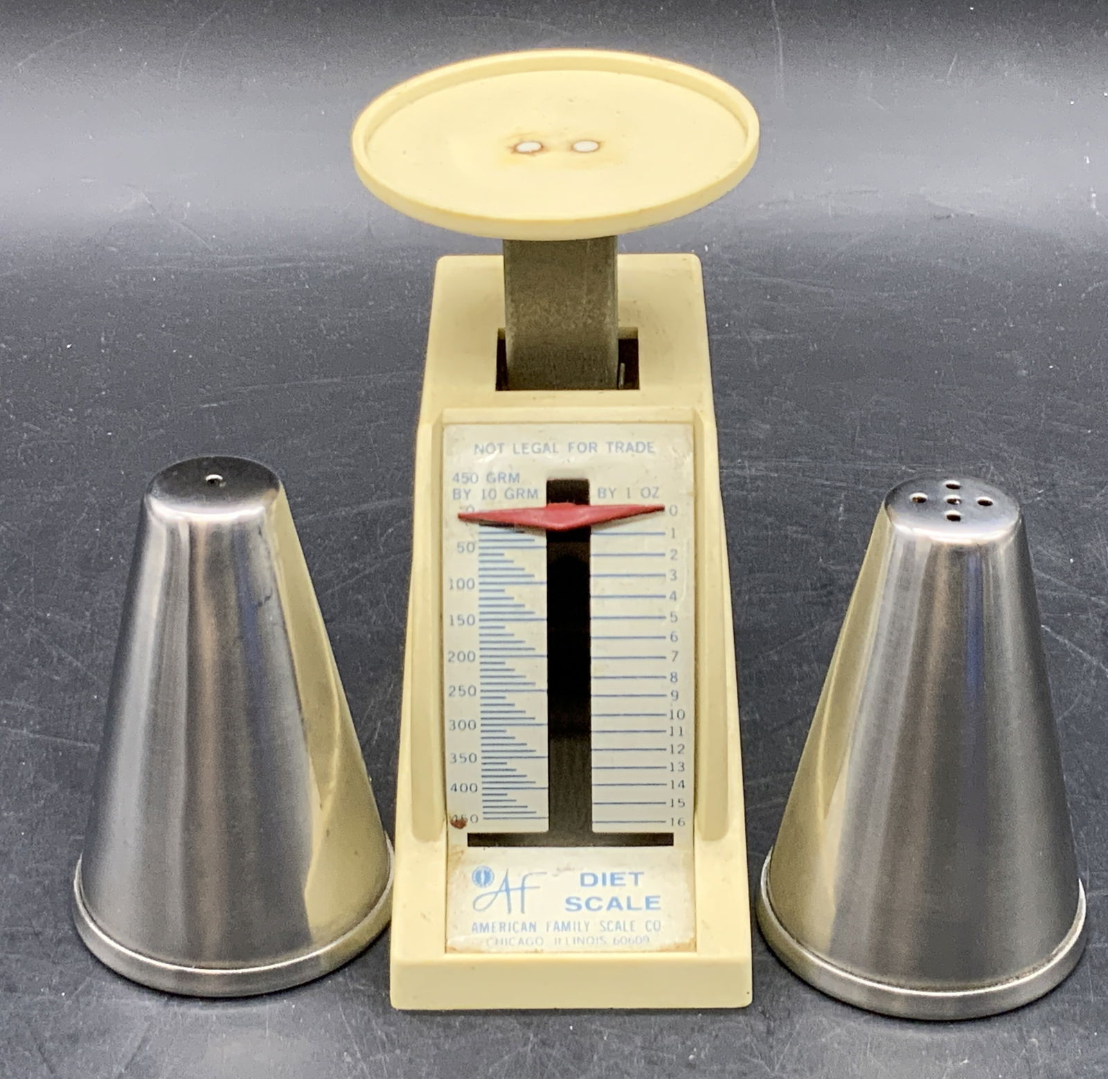 Lot 3 Vintage Shakers & Kitchen Scale, Kitchenware: Vintage American Family Scale Co. Diet Scale and two stainless steel shakers. Scale measures approx. 4.25H x 4W in. Measured at widest point. Wear consistent with age, use, and exposure. Some residue