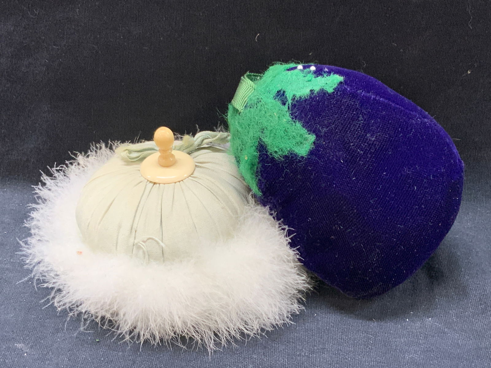 Vtg Pin Cushion & Powder Puff: Vintage home accessories. 1 pin cushion in the shape of an eggplant and 1 off white leather powder puff with possibly bakelite handle, largest is 4 inches wide. Moderate blemishes and wearing from pre