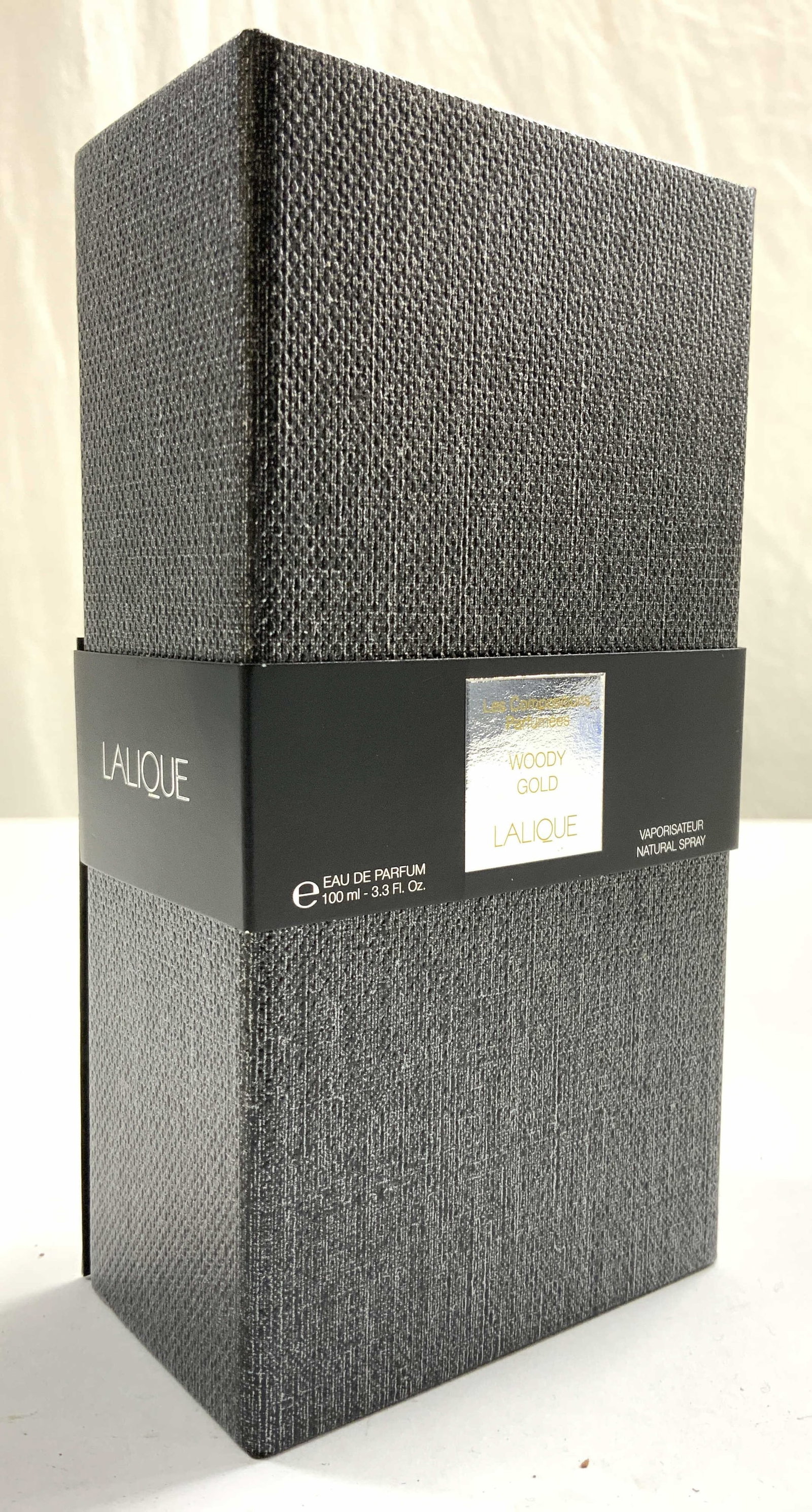 LALIQUE WOODY GOLD Eau De Parfum 3.3 FL Oz W Box: Trademark reads LALIQUE. Box is dark grey toned with black label around box. Includes a 3.3 Fl oz 100 ml bottle. Appears to be New In Packaging. Box measures approximately 6.25 inches tall 3.25 inches