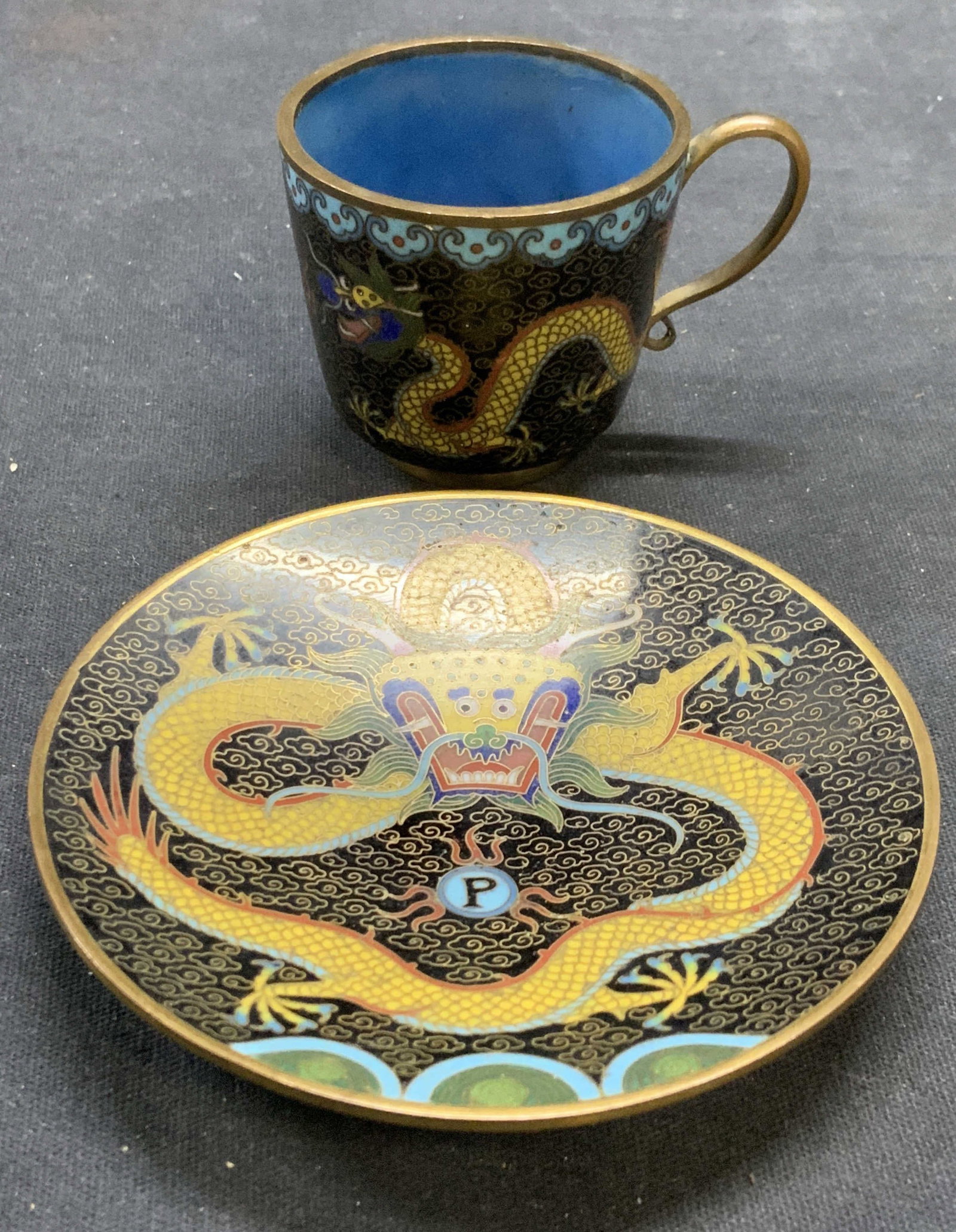 Cloisonne Dragon Demitasse Cup & Saucer: Vintage cloisonne dragon motif demitasse cup and saucer. Enamel over brass. Saucer measures approx. 3.5 inches wide. Cup measures approx. 2 x 1.75 inches. Both piece have some surface wear including s
