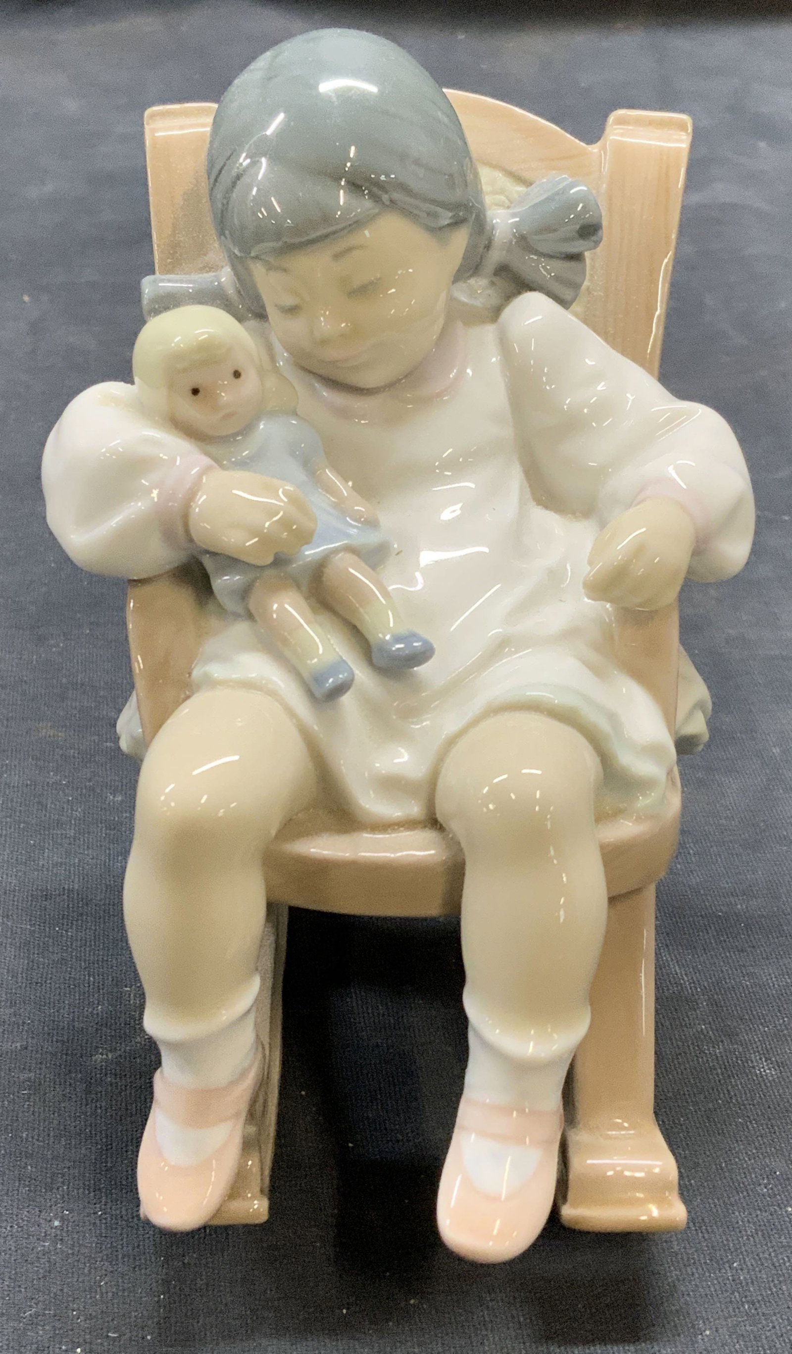 Lladro Porcelain Child Rocking Chair Figural Spain: Lladro porcelain child and rocking chair figural in brown and white. Trademarked to underside. Made in Spain. Measures approx. 3.25 x 4 x 4.5 inches. Some surface wear consistent with exposure. Lladro