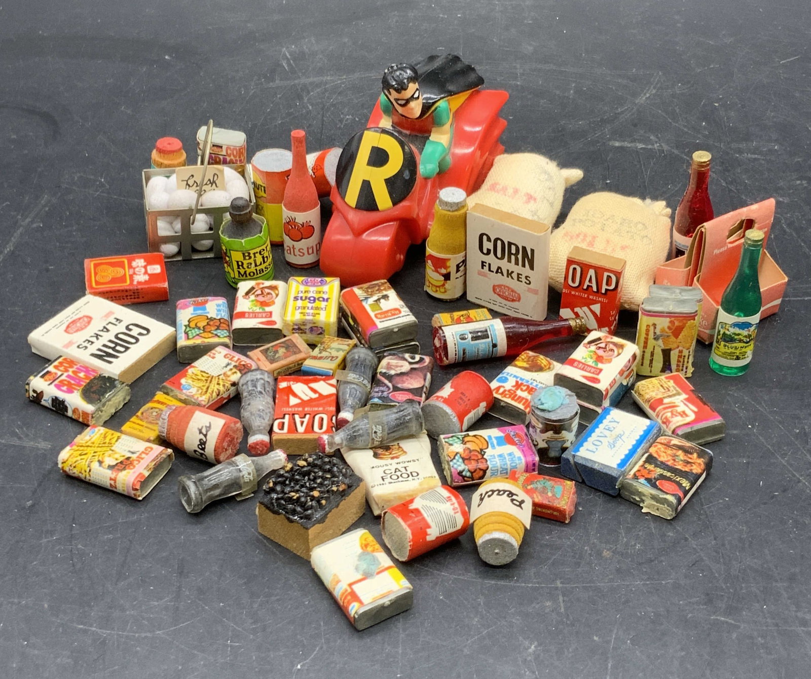 Group Lot Dollhouse Food Miniatures & More: A group lot of dollhouse food miniatures and a 1993 Robin on his motorcycle figural. Pieces are crafted from cardboard, paper, plastics, and more. Robin measures approx. 2H x 2.75W in. Surface wear, d