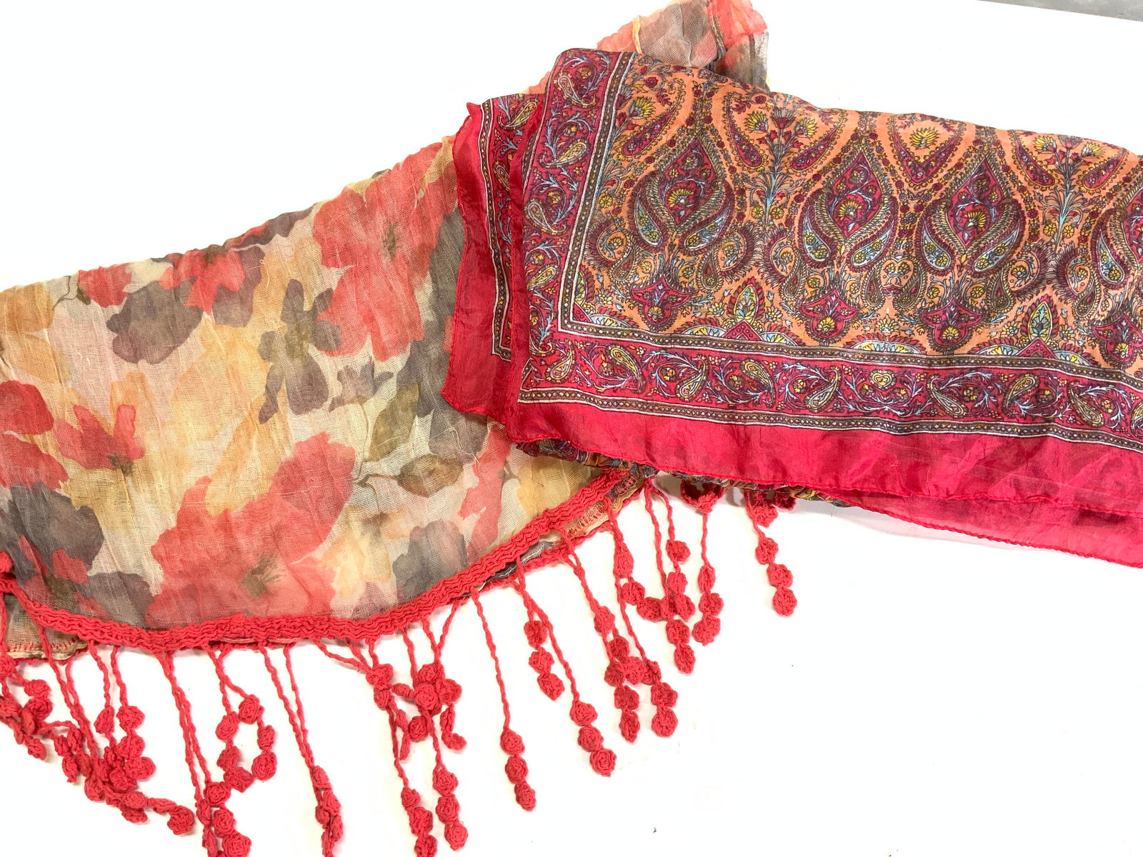 Lot 2 Paisley & Hand Crochet Tassel Scarves/ Shawl: 2 long fashion scarves. One has a gauzy floral sheer fabric with hand crochet tassels added to the ends. Colors or red, black, and saffron. Measures 22 in. Wide, 70 in. Long. Delicate Silk paisley sca