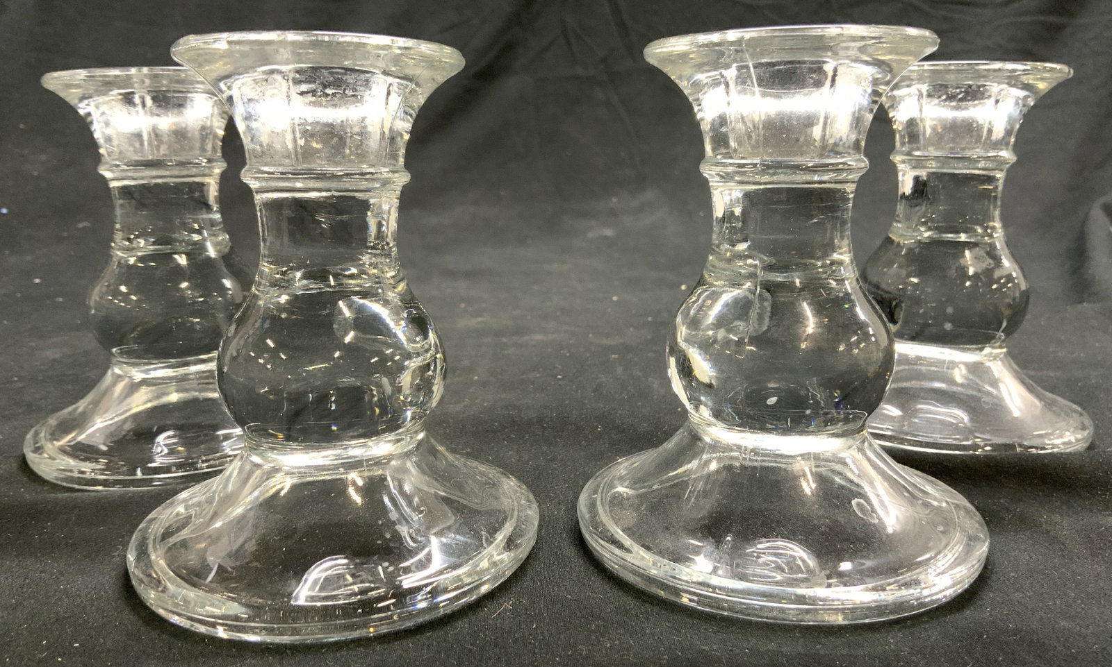 Set 4 Glass Tabletop Candlesticks: Lot includes 4 candlesticks. Each are glass. Candlesticks each have circular shaped bases. Each candlestick measures approx 4 inches tall 3.25 inches wide. Candlesticks, glass candlesticks, set of gla