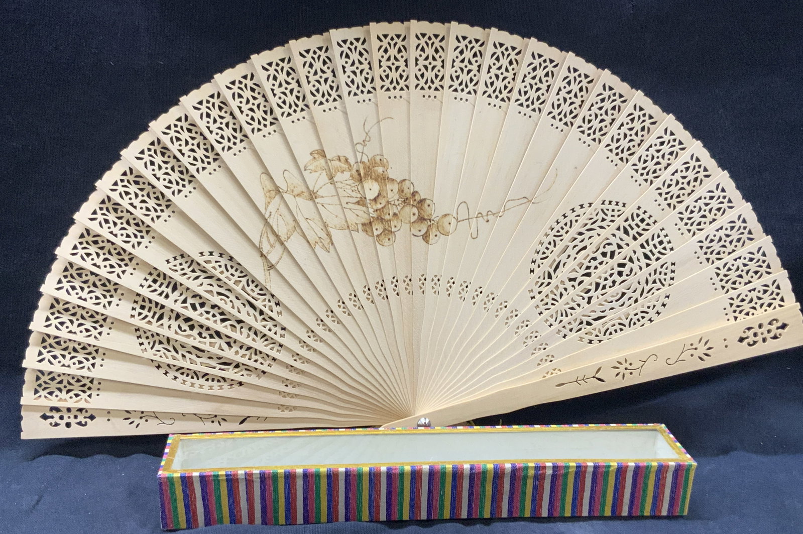 Open Work & Pyrogravure Wooden Fan W Box: Tan toned cut / openwork wooden fan with hand burned design of grapes in the center, comes in original case with multi colors on lid with glass top. Approx 8 inches long and 14 inches wide, case being