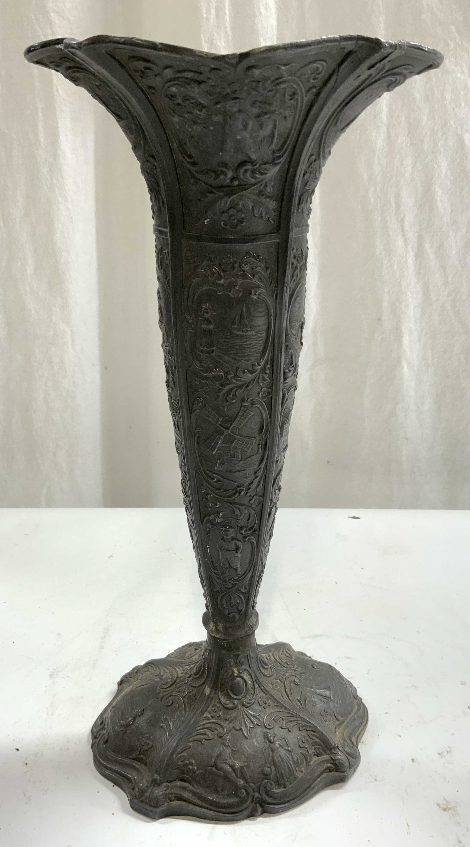 Vintage Ornate Cast Iron Trumpet Vase: Vase is black toned appears to be cast iron. Vase has trumpet form. Piece has intricate ornate detail with scroll and leaf detail, windmill and boats and sea. Vase measures approximately 13.25 inches 