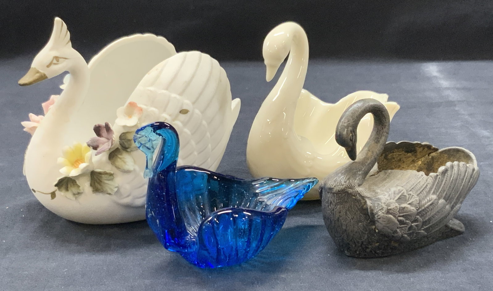 Lot 4 Vtg Porcelain, Glass Swan Figures: Lot of 4 vintage swan figures, 1 porcelain with flowers and painted pained face. 1 marked Lenox on underside, 1 blur glass and 1 silver plated brass figure. Largest being 4 x 5 inches Moderate wearing