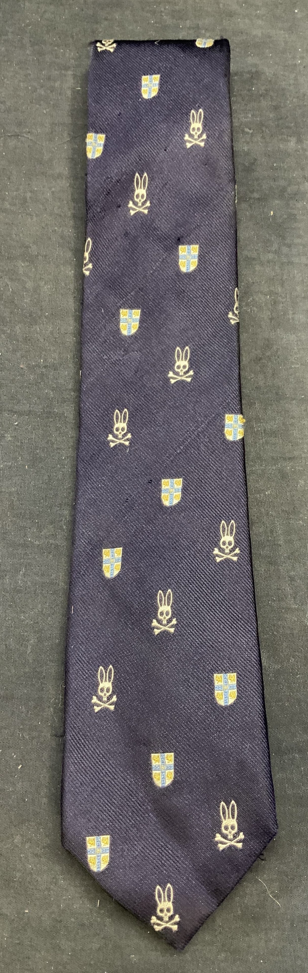 Psycho Bunny Blue Silk Embroidered Tie USA: Psycho Bunny blue silk embroidered tie with skull and shield motif. Hand made in USA. Measures approx. 62 inches long, some wear to material including pulling observed. Psycho bunny, psycho bunny tie,