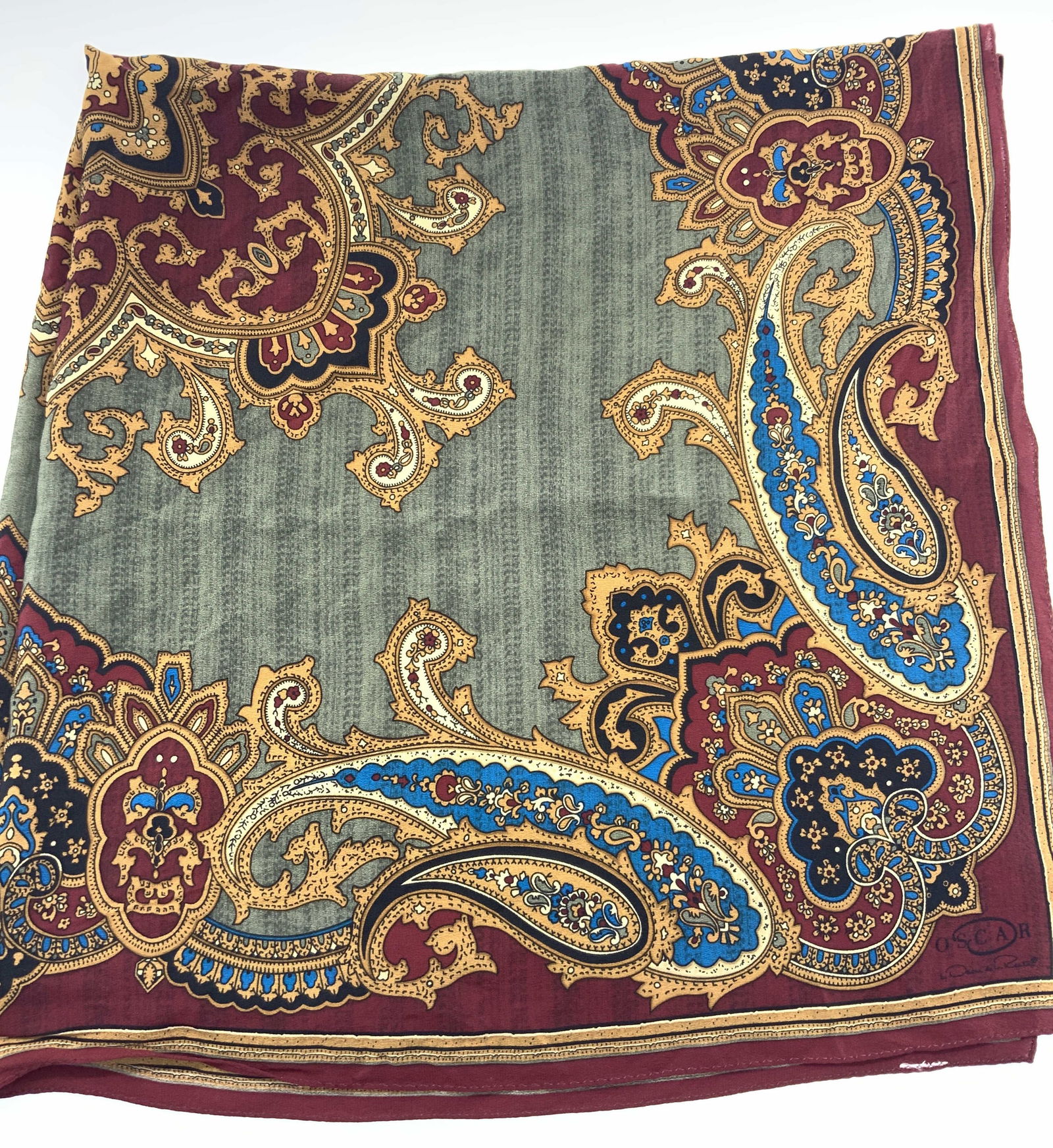 Oscar De La Renta Silk Paisley Scarf: Marked on corner Oscar de la Rental silk scarf with hand rolled edges and paisley designs in red and blue against a green base with gold toned scroll designs. Approx 32 x 32 inches Moderate wearing to
