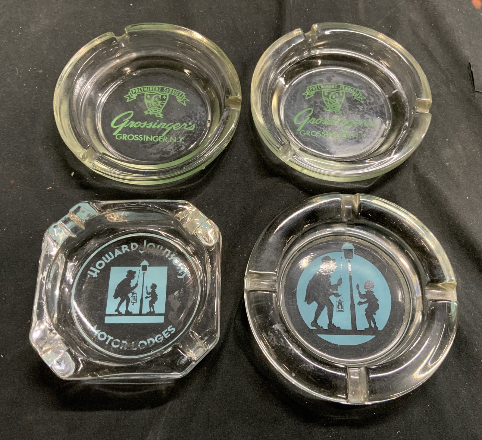 Lot 4 T Marked Glass Trinket Dishes Ash Trays: Lot includes 4 ash trays, 1 trademarked Howard Johnson Motor Lodges, 2 trademarked Grossingers, 1 with male and boy figure near street light. Largest dish measures approximately 4.5 inches diameter. A
