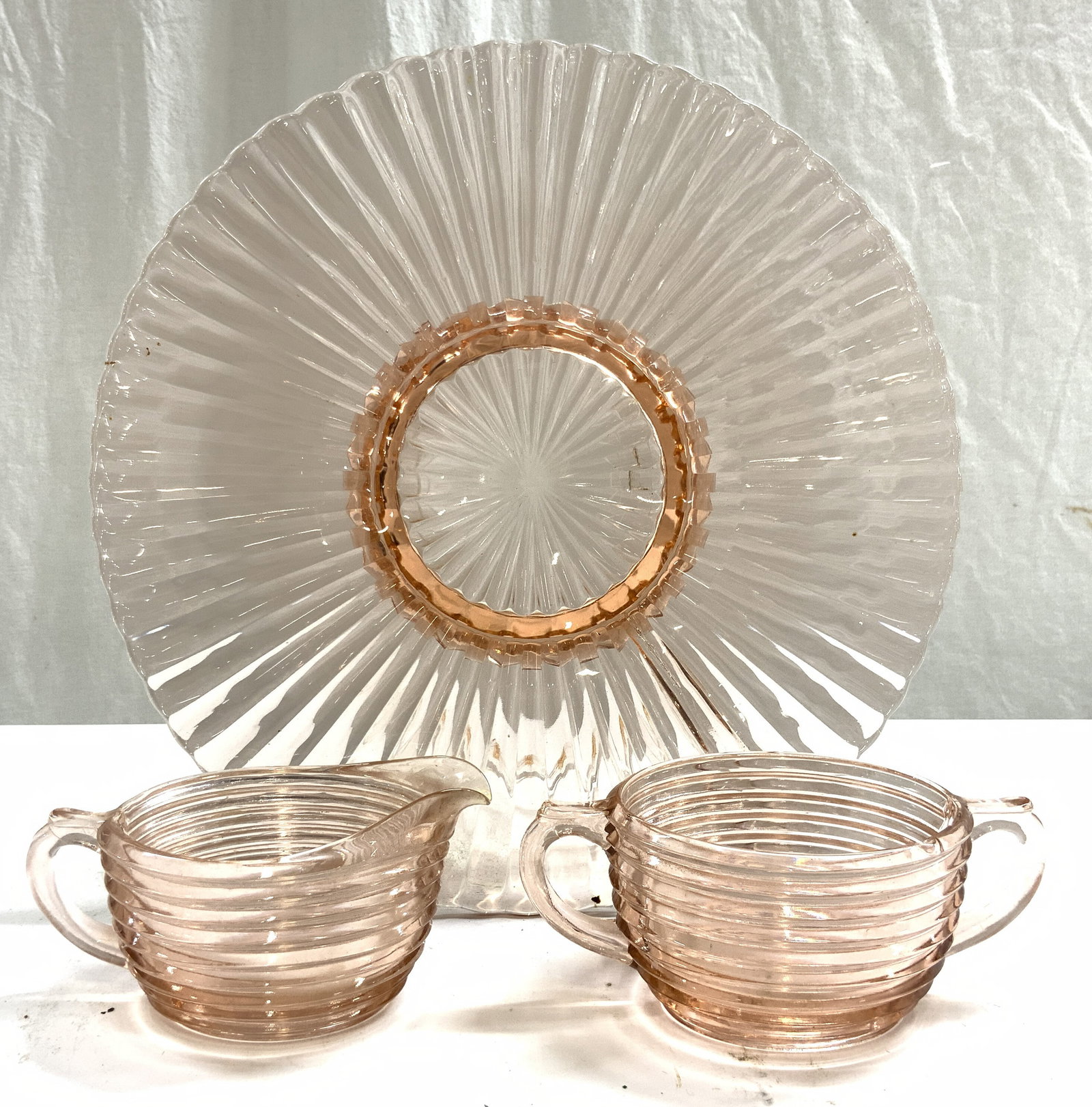 Ribbed Depress Glass Plate, Sugar & Creamer Pink: Lot includes 1 plate, 1 sugar dish & 1 creamer dish. Each piece is pink toned with ribbed exteriors. Serving plate is footed. Plate measures approximately 12.25 inches diameter. Plate, sugar dish, cre