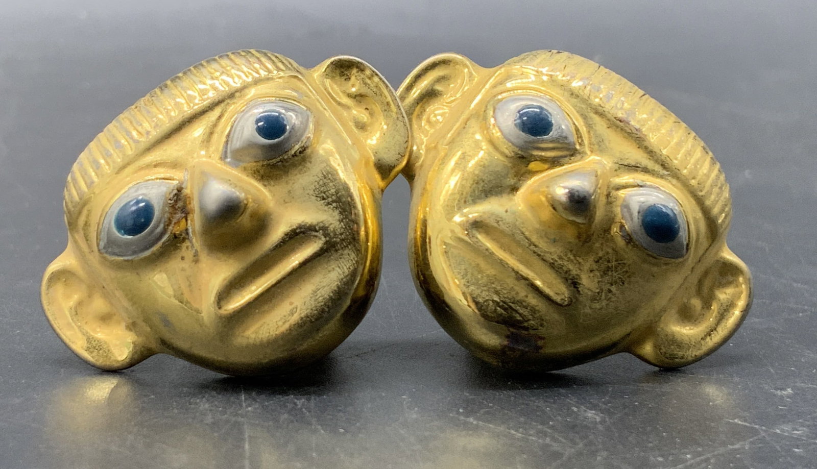 SIPAN Gold Tn Metal Face Figural Clip On Earrings: Vintage gold tone metal face figural earrings featuring silver tone and blue enamel eyes. Clip on backings to reverse, marked SIPAN to reverse. Measures approx. 1.25W x 1L in. Some discoloration and s