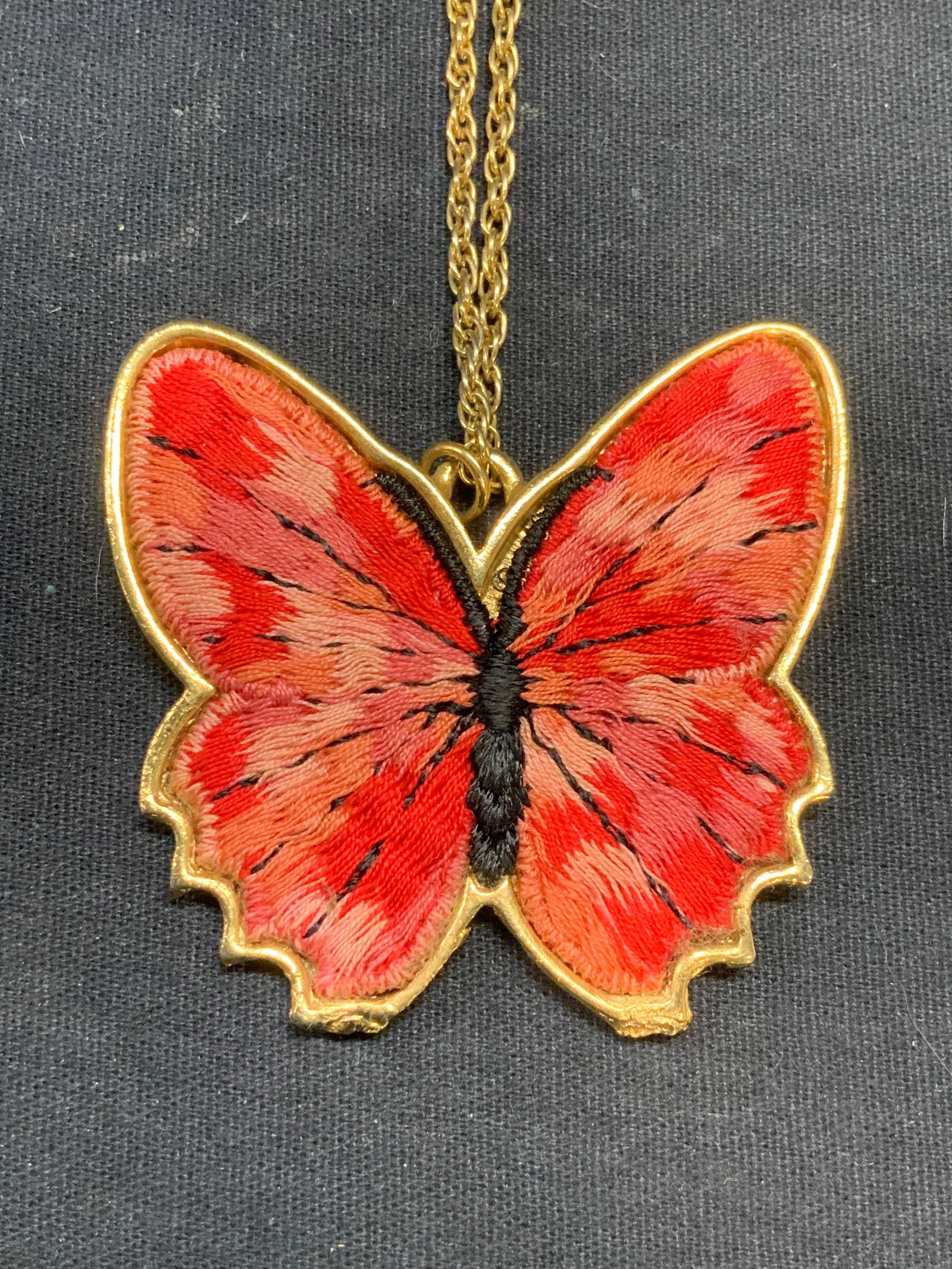 BJ Gold Tn Embroidered Butterfly Pendant Necklace: BJ Gold tone necklace with red and pink toned embroidered butterfly motif pendant. Signed on pendant. Drop length approx. 11.5 inches. Pendant 2.25 x 2.25 inches. Some surface wear including scratchin
