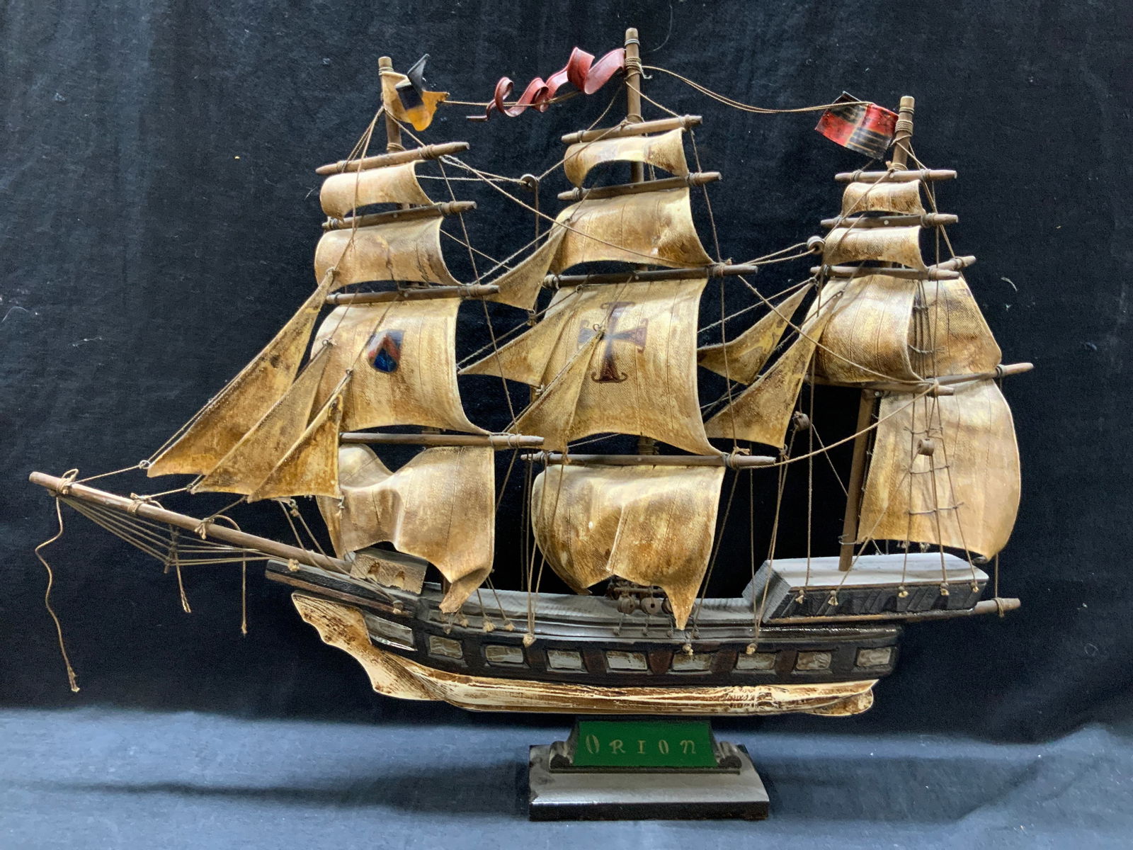 Orion Carved & Hand Painted Ship Model: Carved wooden ship model, painted on side Orion. Hand painted with bronze tones and white undersides and sails to ship crafted with canvas and hand painted iron crosses. Approx 17 inches tall 22 inche