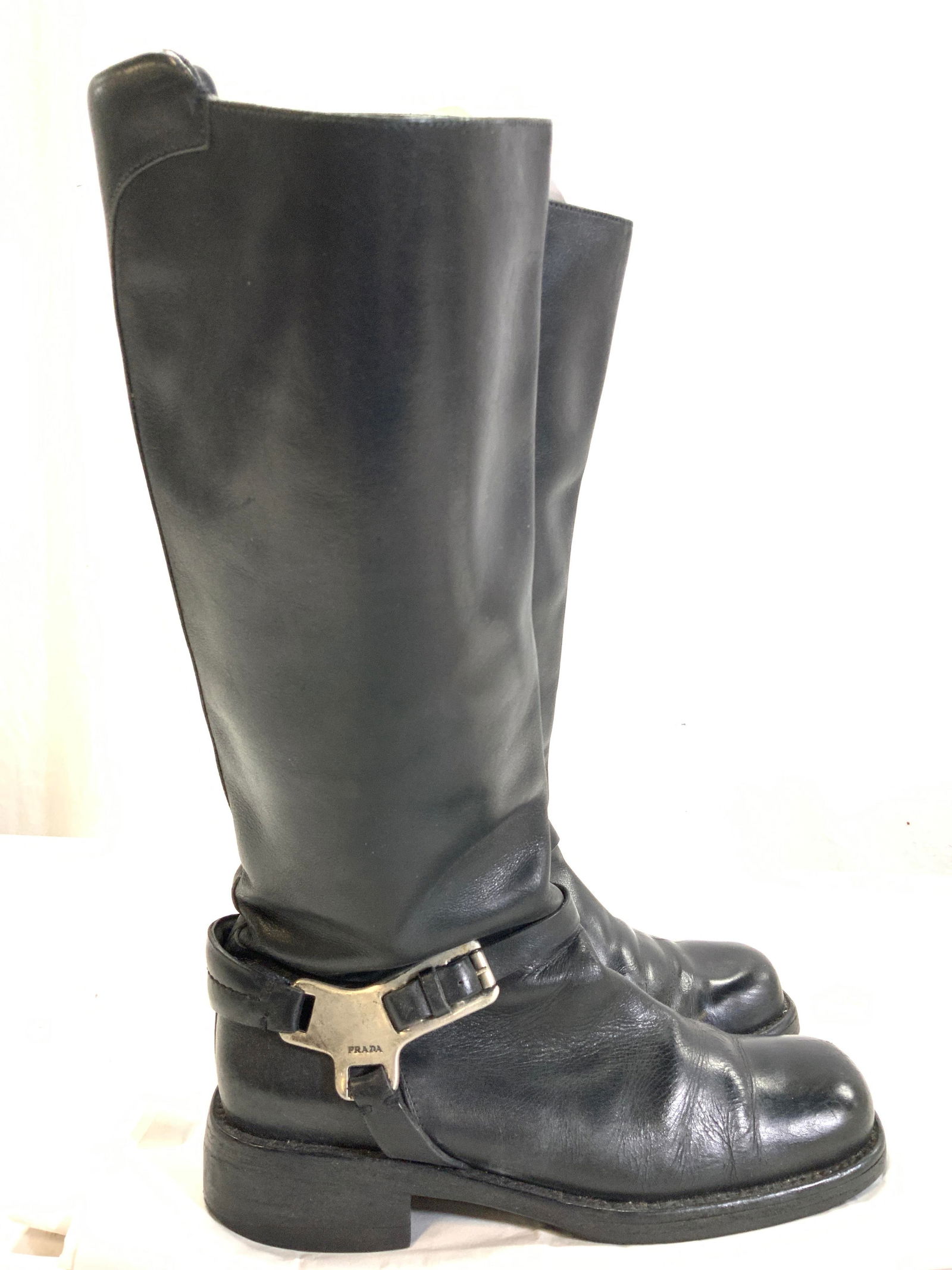 PRADA Black Leather Vtg Casual Knee Boots, ITALY: Signed Prada Vintage black leather books with flat 1.5 in. heel, 15 in. Ht. Adjustable buckle with metal accessory around ankle. Size 38. Made in Italy. More of a rectangular foot shape. Maintains lea