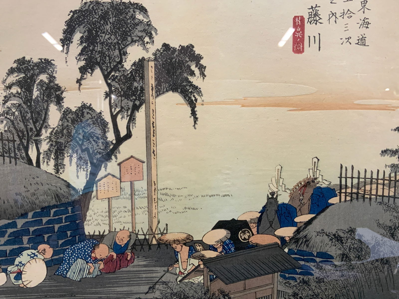 Hiroshige Utagawa Tokaido 53 Station Block Print: Stamped on edge with black, along with black calligraphy on edges. Depicts a group of people bowing while a nobility procession comes through the street. Framed in a black wooden frame with off paper