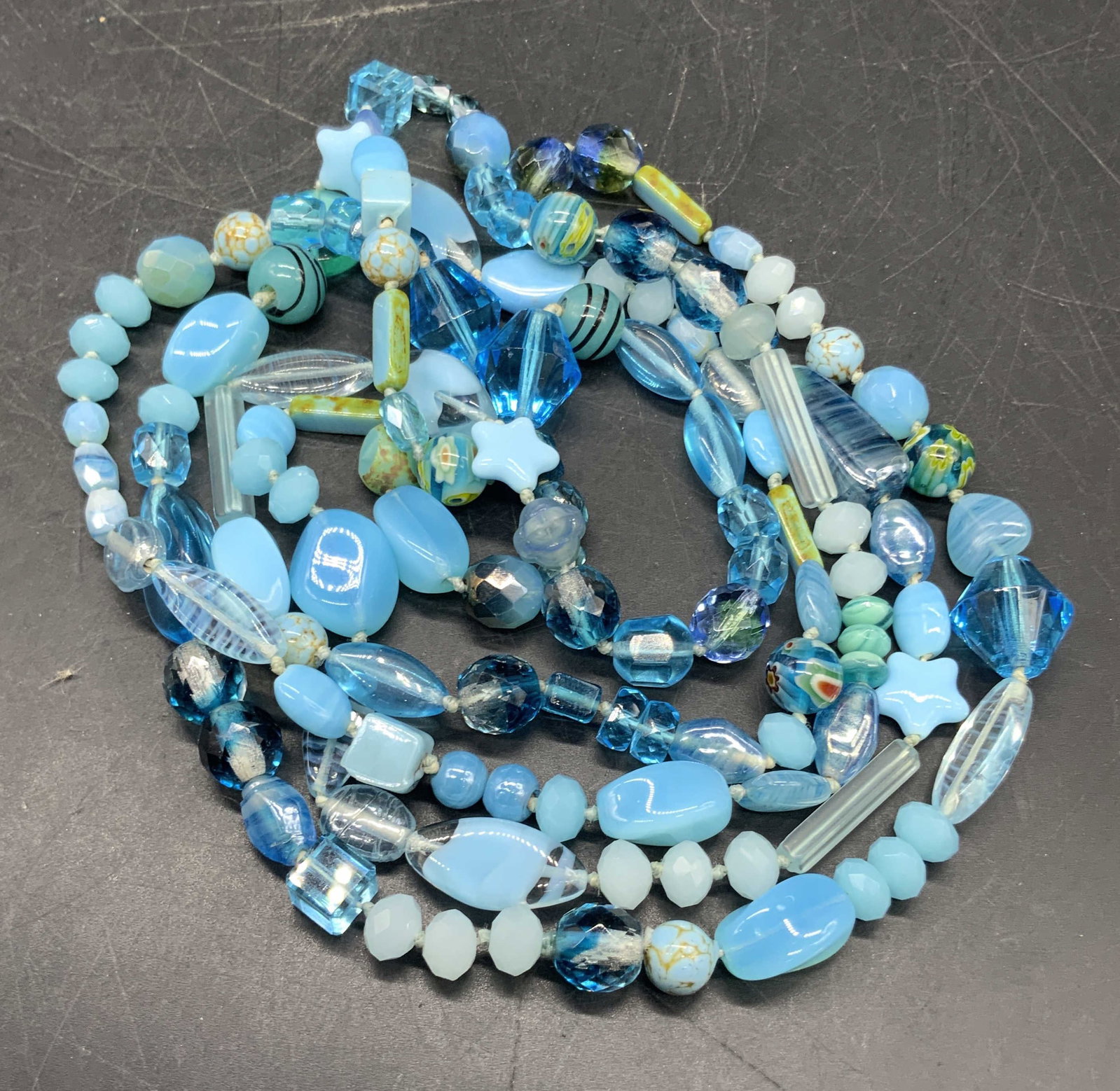 Blue Beaded Lariat Length Necklace: A blue beaded lariat length necklace comprised of composite and glass beads. The beads are various shapes, sizes, and hues of blue. Some other colors interspersed throughout. Drop length measures appr