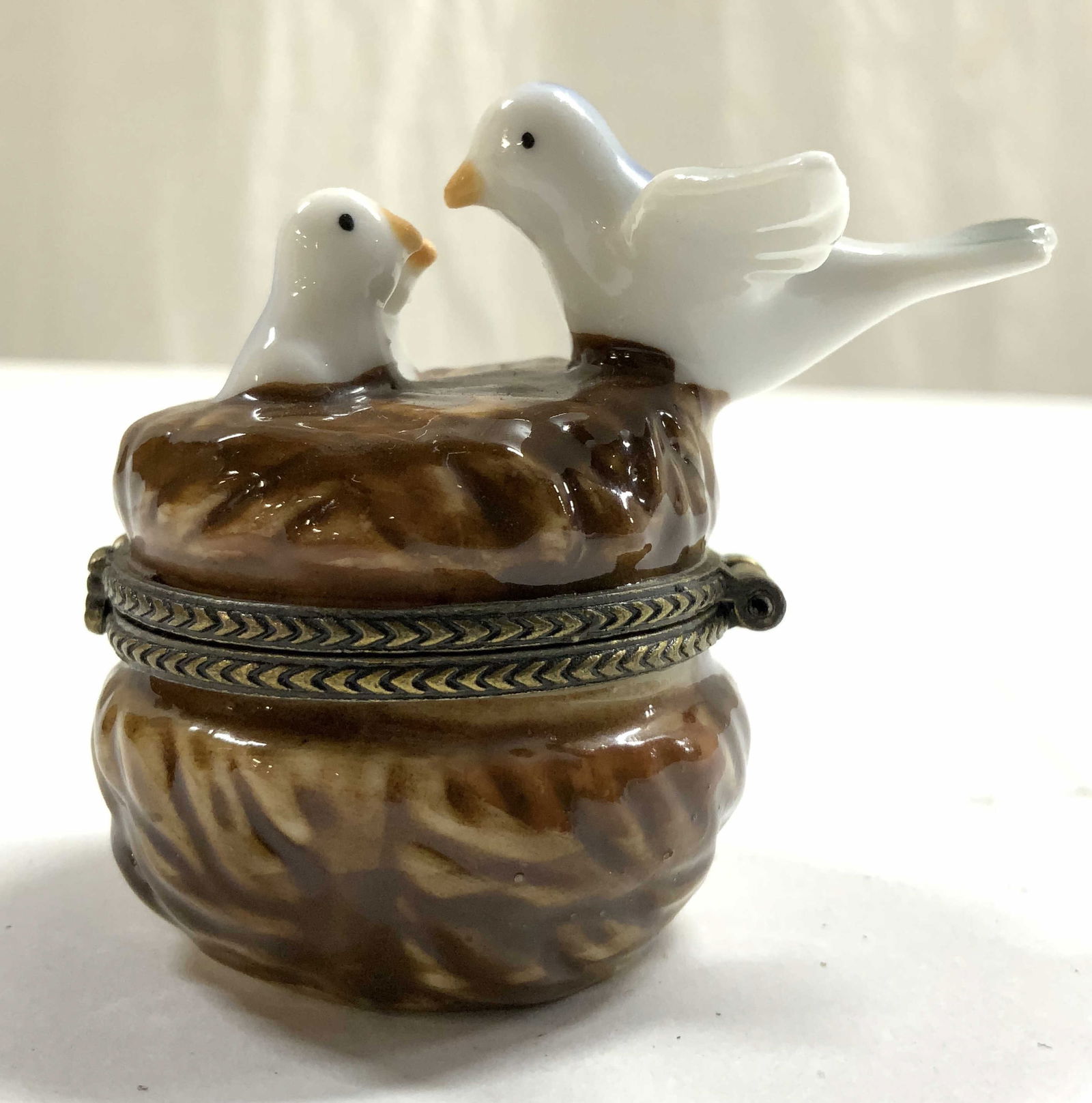 Porcelain Bird nest Pill Box W Lid: Pill box is porcelain. Piece has bird nest form with mother and baby birds. Pill box has gilt metal rim & edge to lid. Piece measures approximately 2.5 inches deep 2.25 inches tall 1.75 inches wide. P