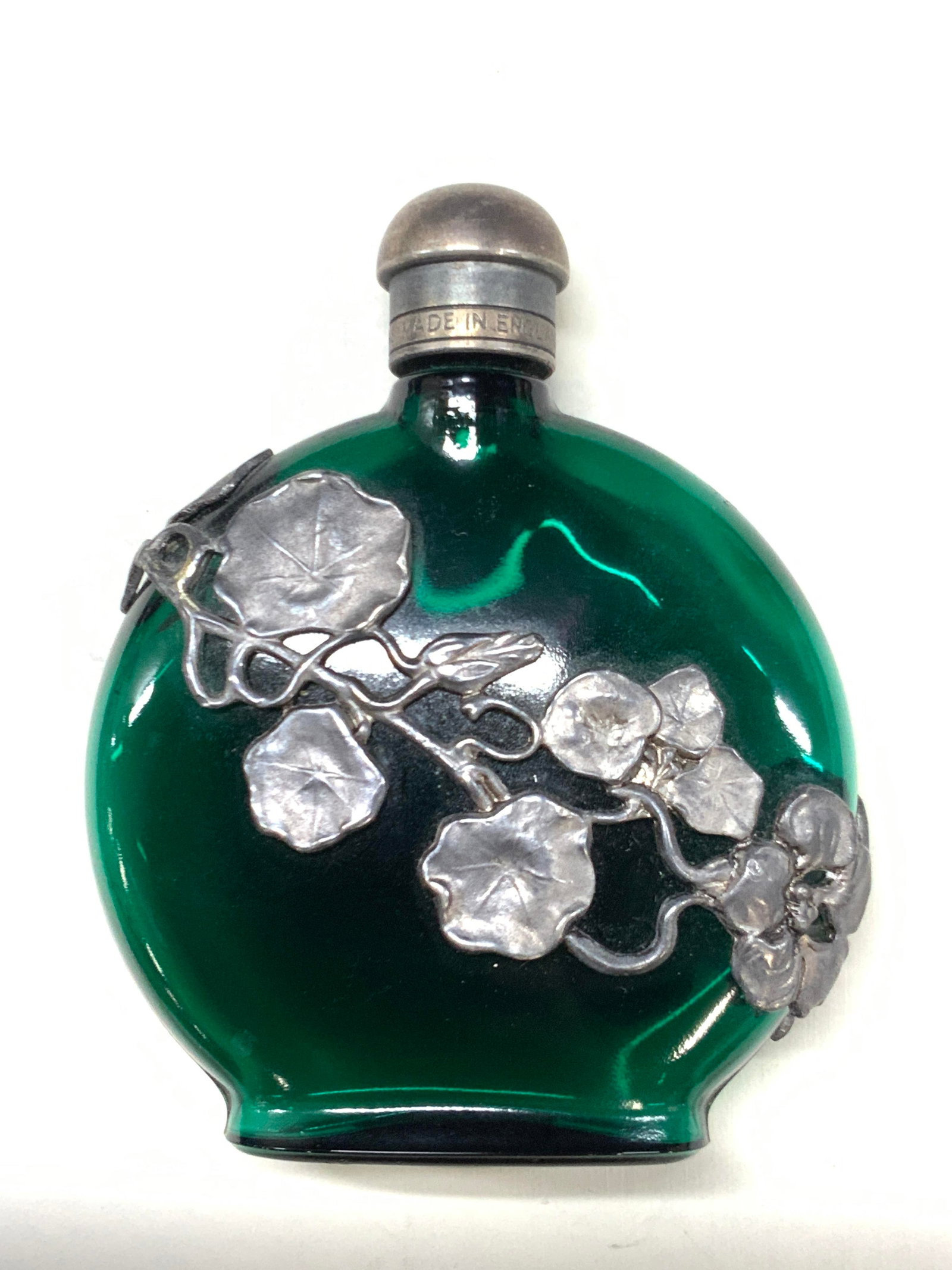 First Impressions Glass Perfume Bottle, England: Marked on cap, first impressions, made in England, green toned glass bottle with silver plated floral motifs across the exterior of the bottle. Approx 4 inches tall and 3 inches wide. Moderate wearing