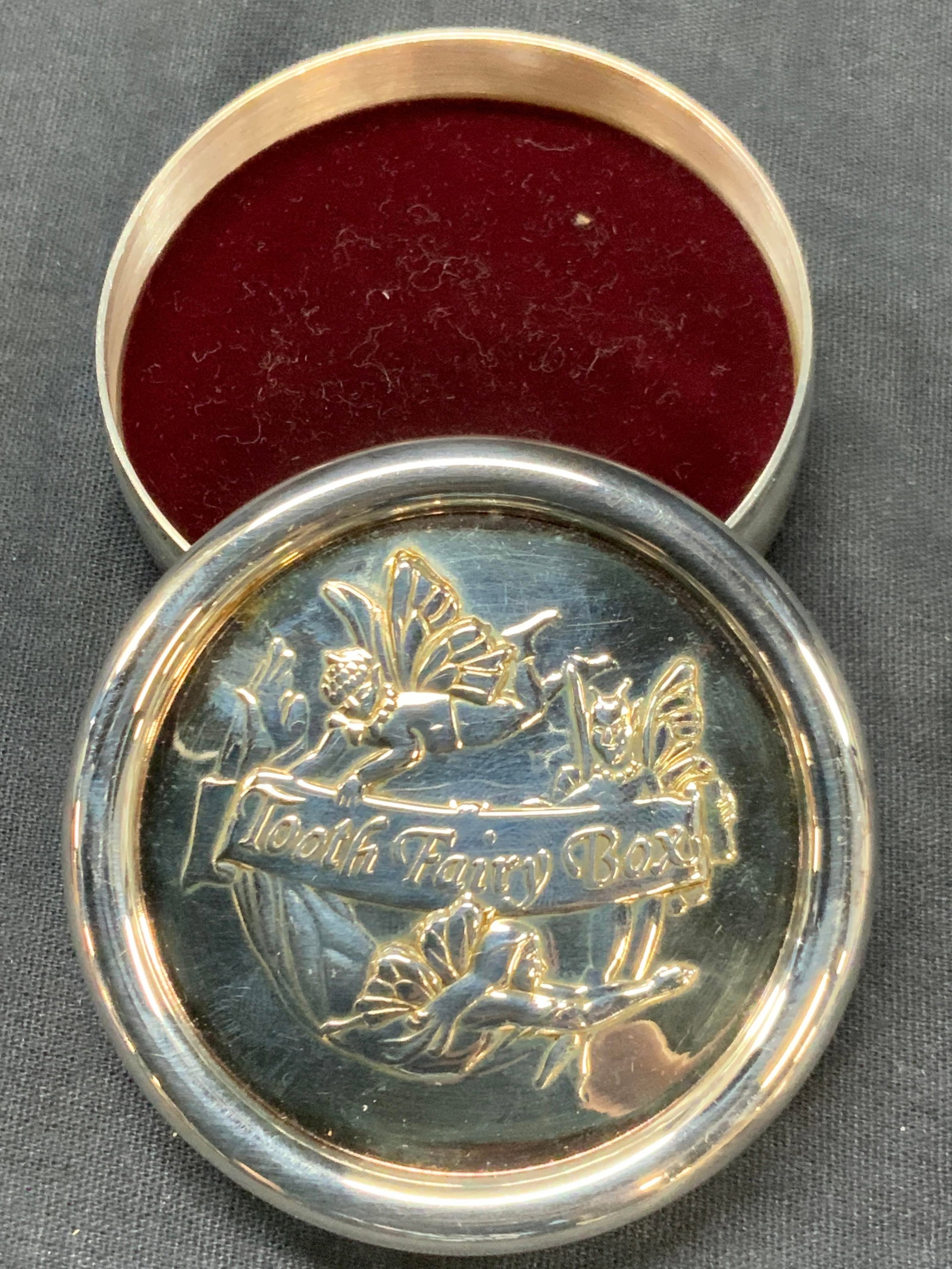 Reed & Barton Silver Plate Tooth Fairy Box: Reed & Barton silver plate tooth fairy Box, embossed on lid with image of a fairies flying. Interior is lined with red velvet. Approx 1 inch tall and 2.5 inch diameter. Minor wearing to plating on box