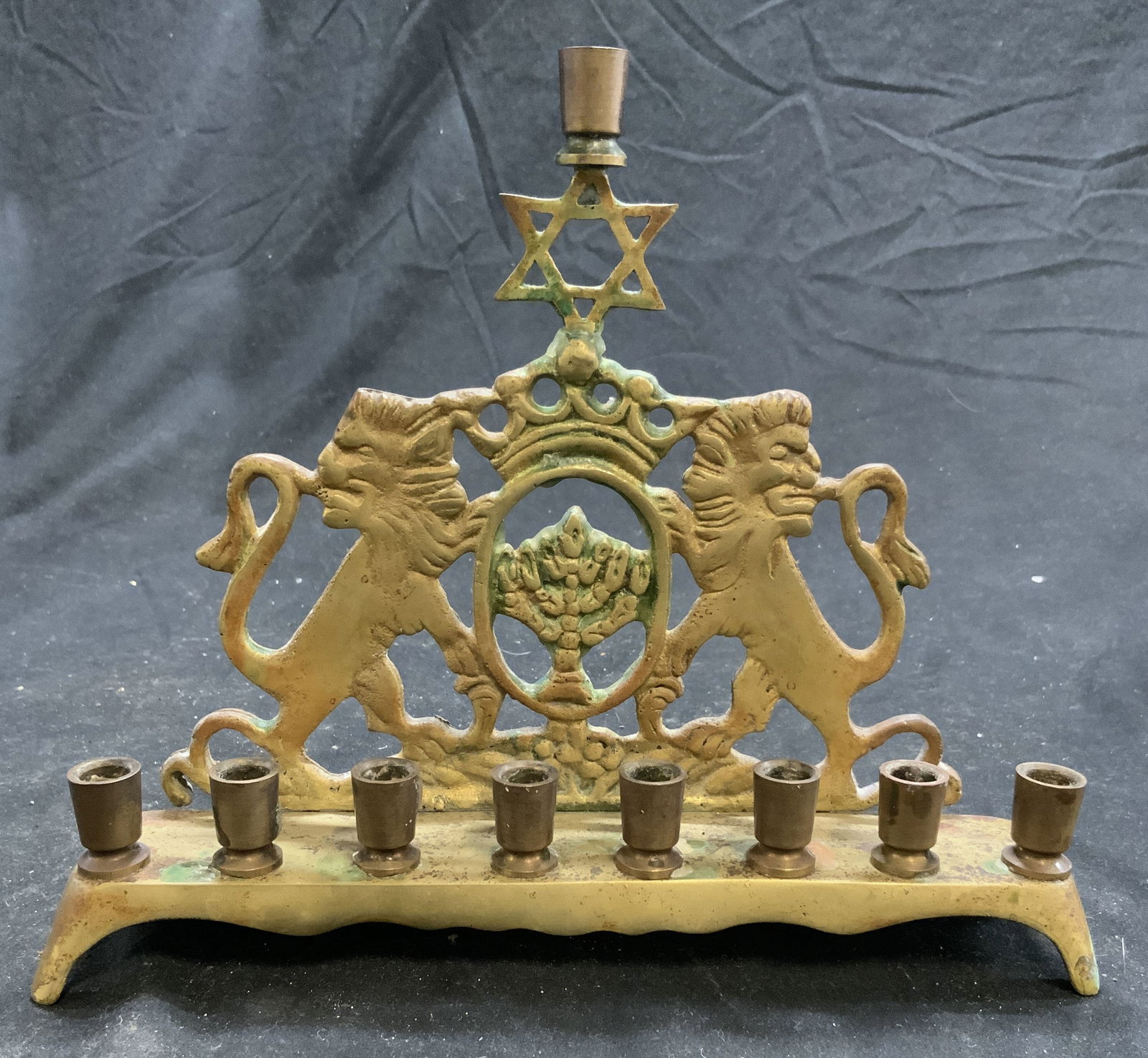Vintage Brass Judaica Menorah W Lion Detail: Menorah is vintage. Piece is gold toned and brass. Menorah has double standing lion detail. Top of piece has Star of David. Menorah is footed. Piece measures approximately 7.5 inches tall 8 inches wid