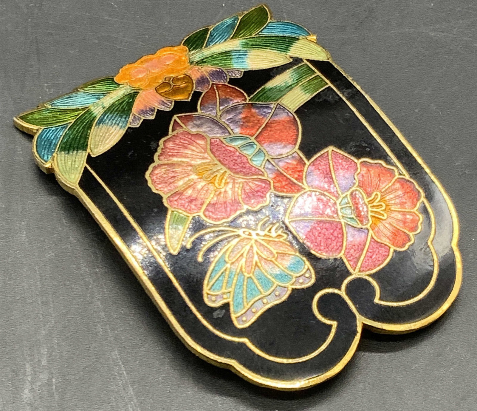 Vintage Asian Cloisonne Floral Belt Buckle: A vintage Asian cloisonne belt buckle decorated with multicolored florals, foliage, and butterflies. Measures approx. 2.5W x 1.75L in. Patina present. Some surface wear consistent with age and use. Vi