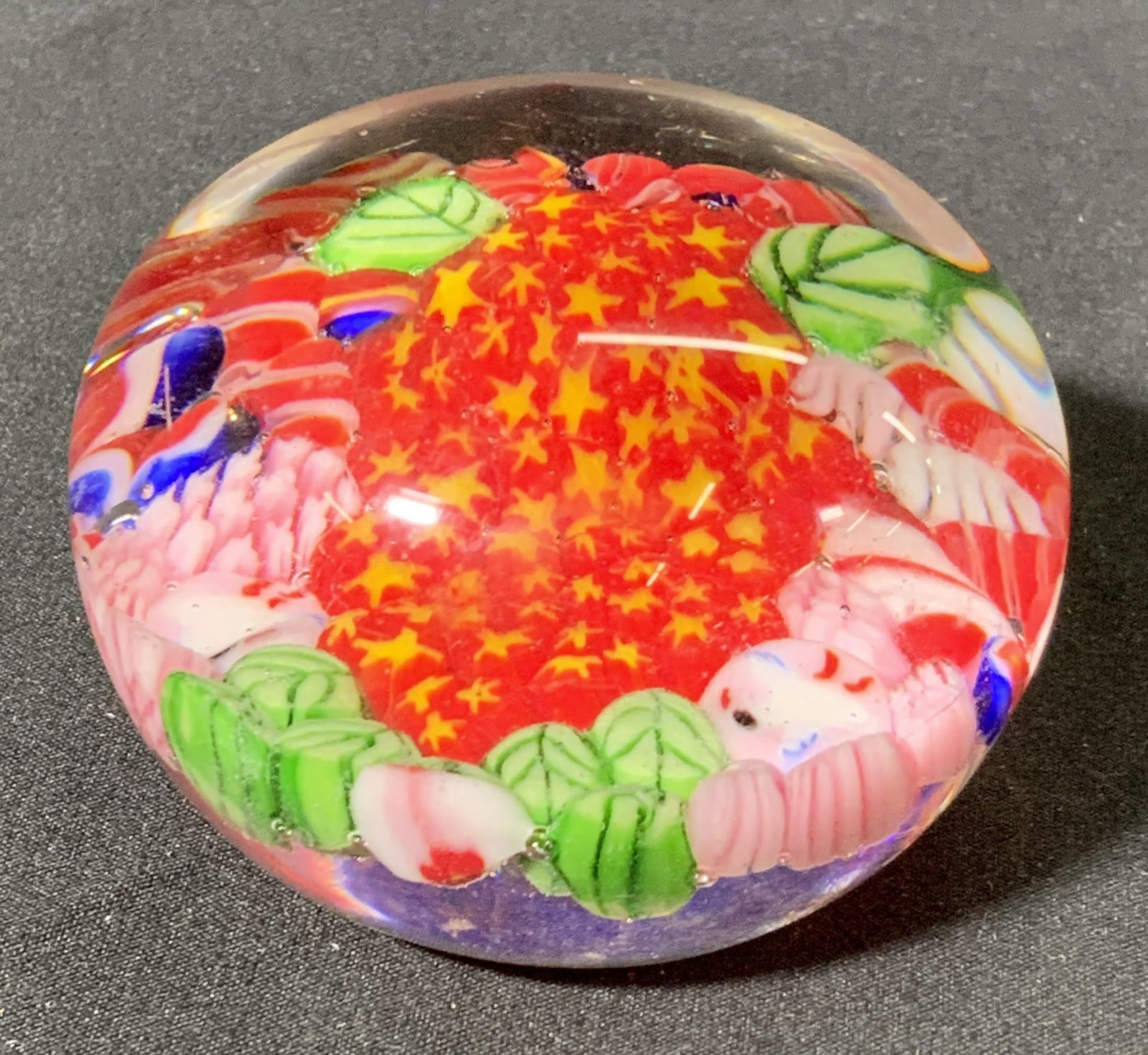 MURANO Style Millefiori Art Glass Paperweight: MURANO style millefiori art glass paperweight with floral inclusions in hues of red, pink, blue, yellow, and green encased in transparent glass. Measures approx. 2.25 inches diameter. surface wear con