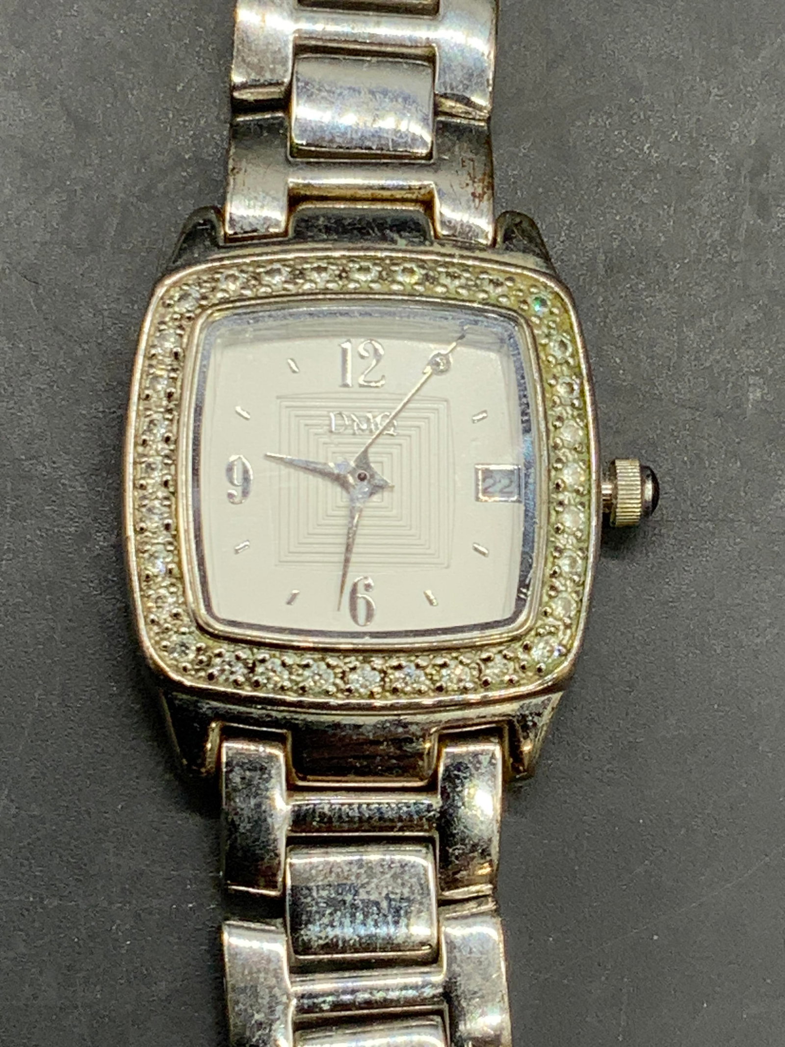 DIAMONIQUE DMQ1016SV Bejeweled Silver Tn Watch: A silver tone metal DIAMONIQUE watch with a box clasp closure. Faceted crystals surround the watch face. Reverse reads DIAMONIQUE DMQ1016SV, Stainless Steel Back, SR621SW. Measures approx. 7.25 inches