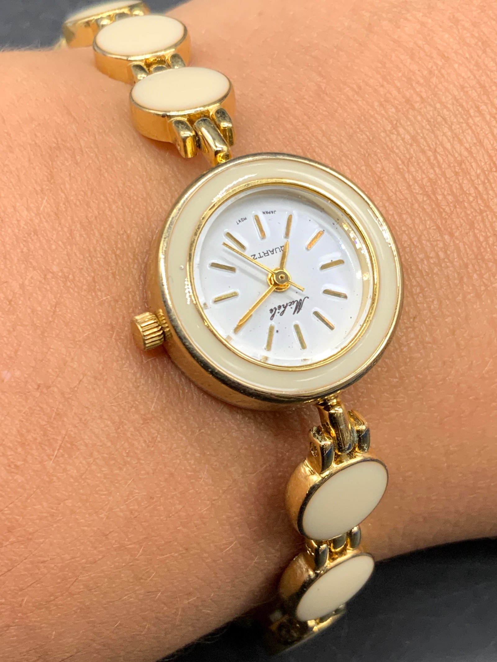 MICHELE Gold Tn Metal Enamel Wristwatch, Jewelry: A gold tone metal watch featuring cream hued enamelwork and a box clasp closure. White clock face reads MICHELE, Quartz, Japan Movt. Reverse reads Stainless Steel Back. Length measures approx. 6.5 inc
