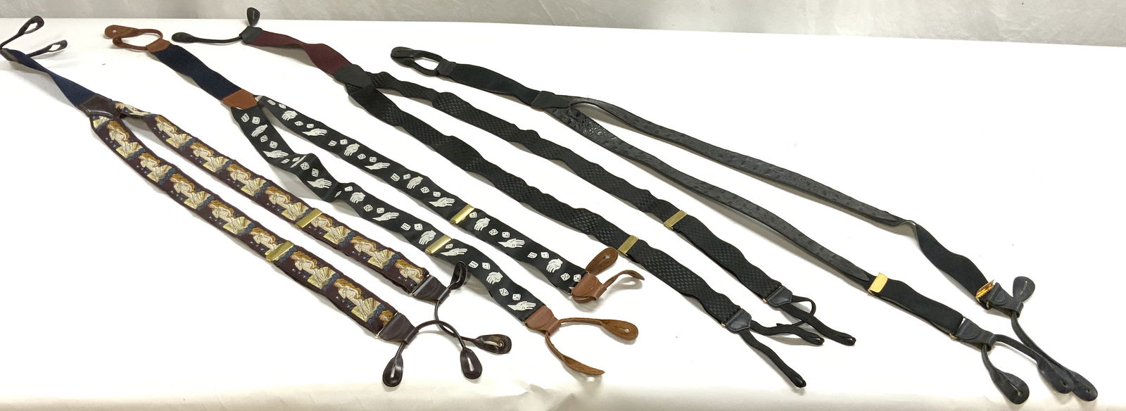 Lot 4 Pairs Of Suspenders: Lot includes 4 pairs of suspenders. 1 leather black toned, 1 black toned with checkered pattern, 1 with rolling dice and hand detail, & 1 with birth of Venus detail. Longest measures approximately 40