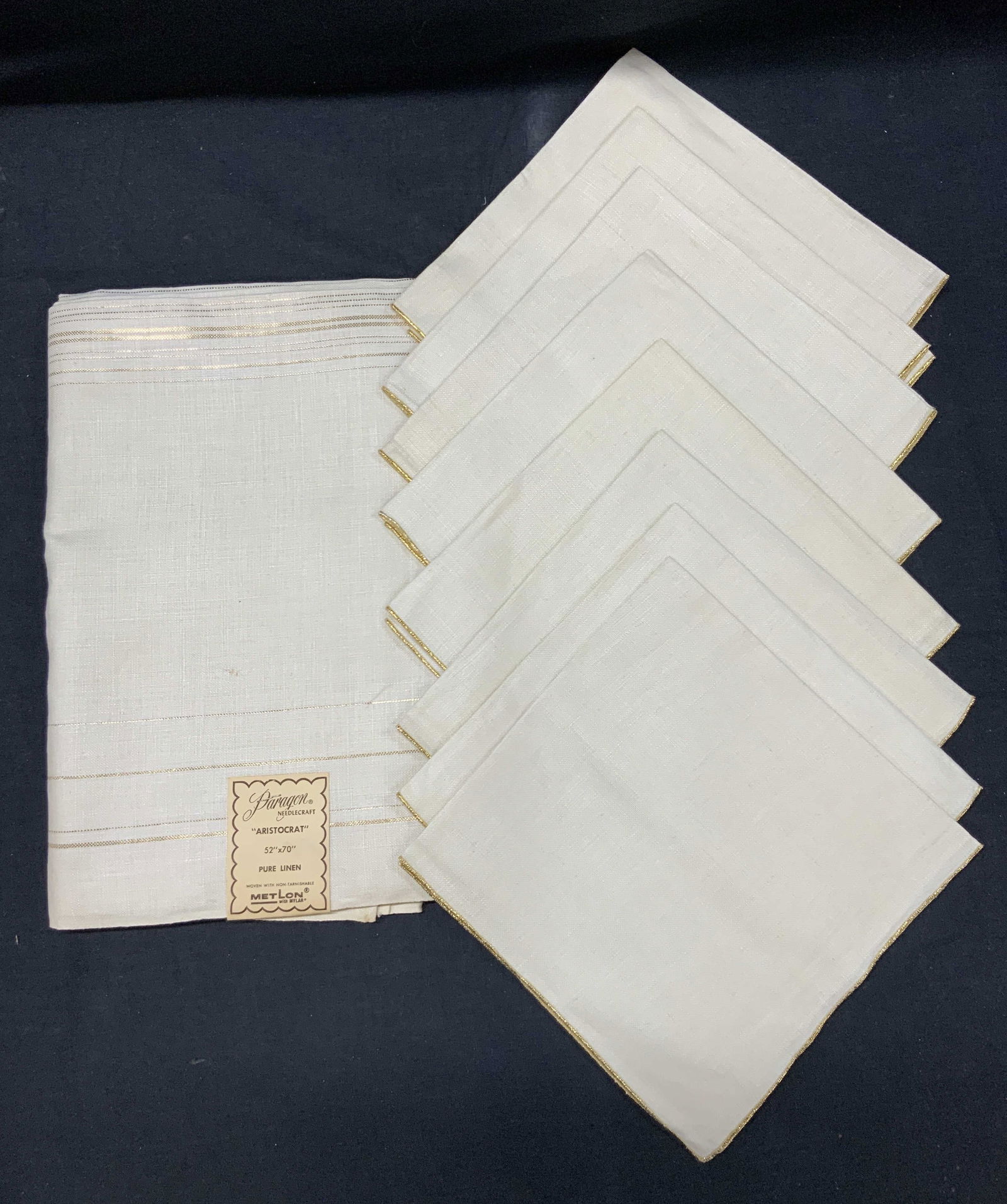 Set 9 Paragon Aristocrat Linen Table Setting, NWT: New with tag, Set of 9 pure linen paragon needle craft table wares. 1 tablecloth at 52 x 70 inches, and 8 linen napkins, all with shimmering gold edges and rims. Approx 17 x 17 inches. Minor wearing t