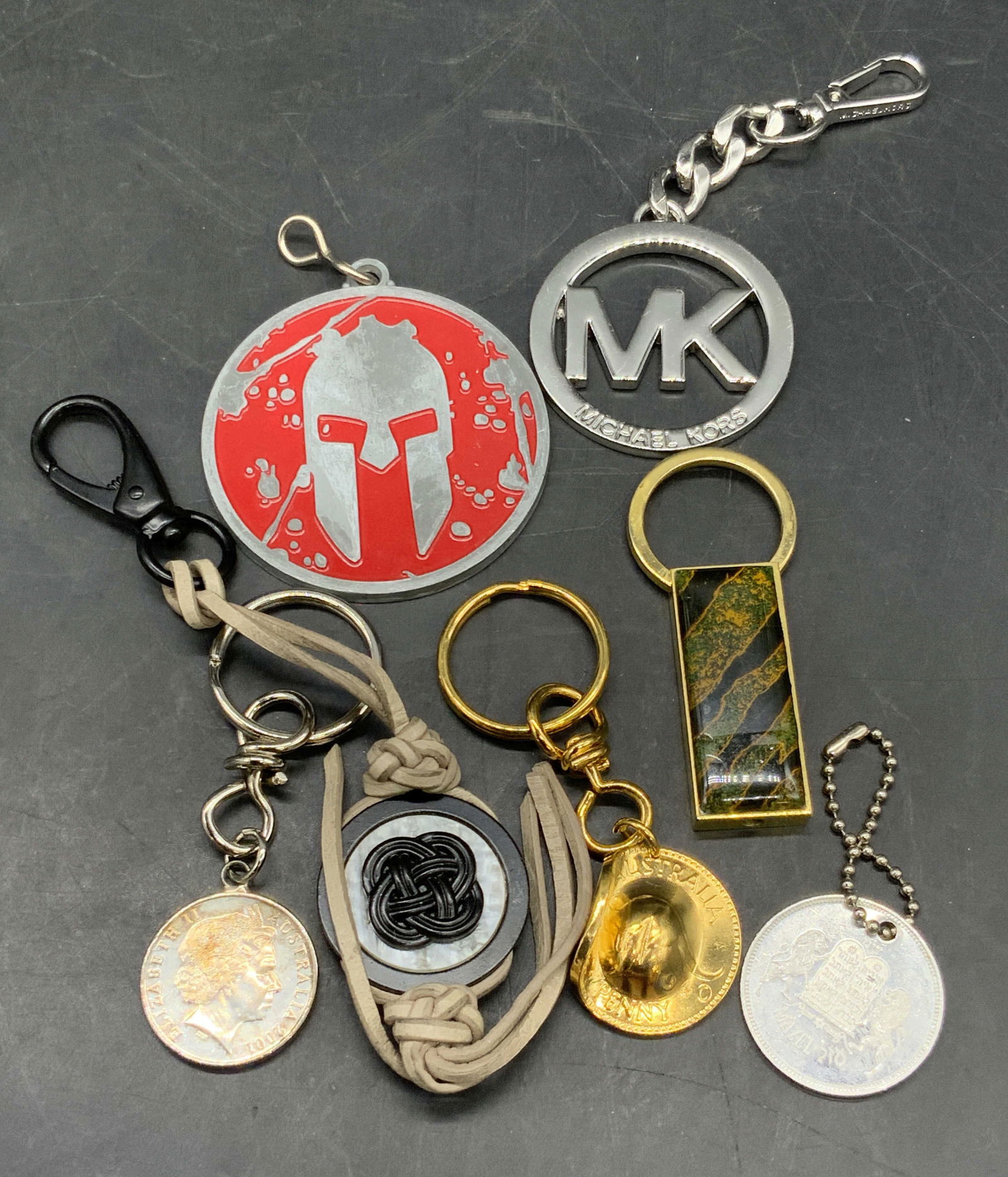 Lot 7 Keychains, Michael Kors, Currency, & More: Seven keychains. Pieces are comprised of metal, currency, composite materials, and more. Lot includes currency turned into keychains, a Spartan Race keychain, a Michael Kors keychain, and more. Michae