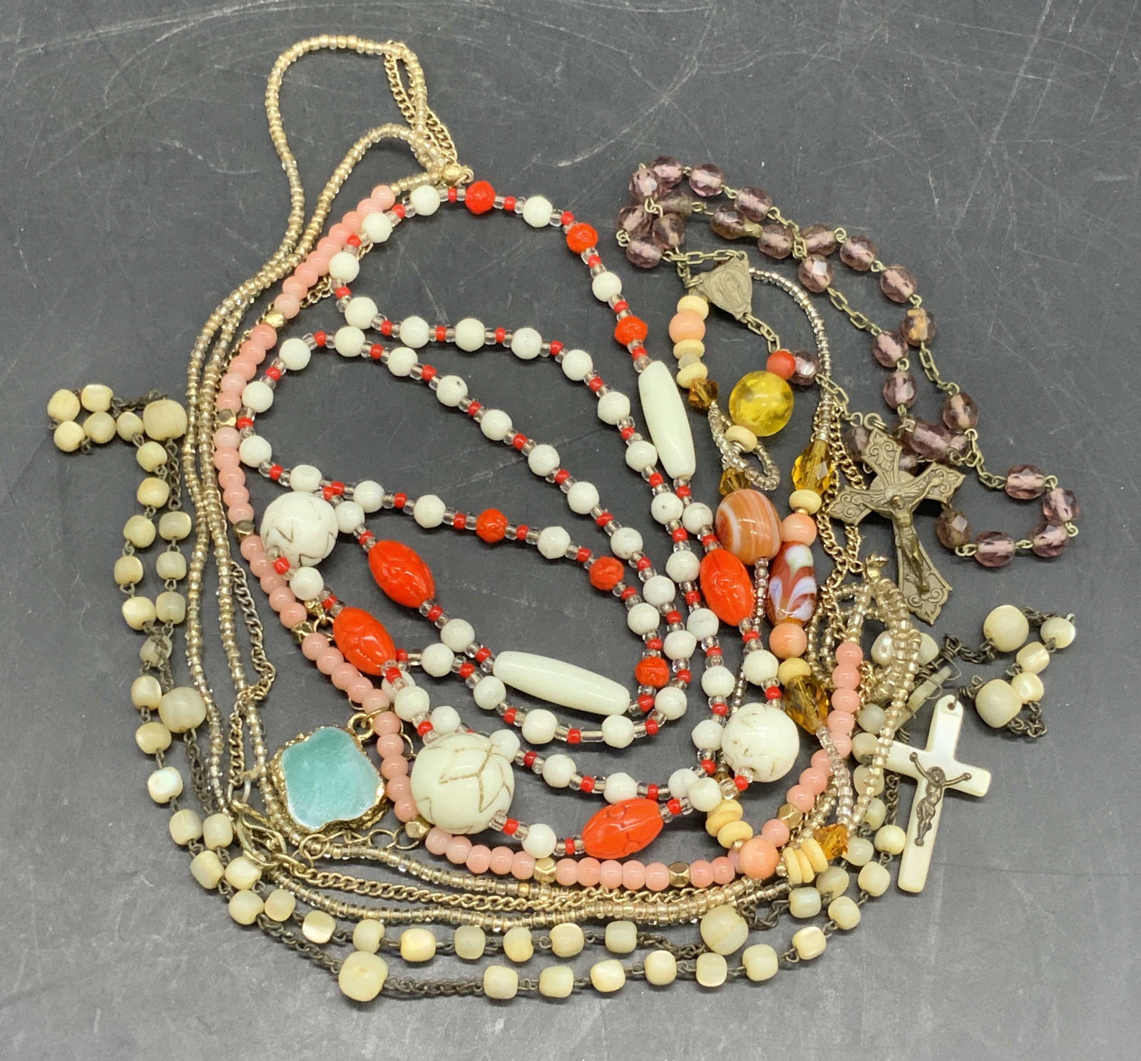 Group Lot Beaded Necklaces, Rosary, & Bracelet: A group lot of necklaces, rosaries, and a bracelet. Pieces feature colorful beadwork. The beads are crafted from glass and composure materials. Multicolored hues throughout the pieces. Metal & composi