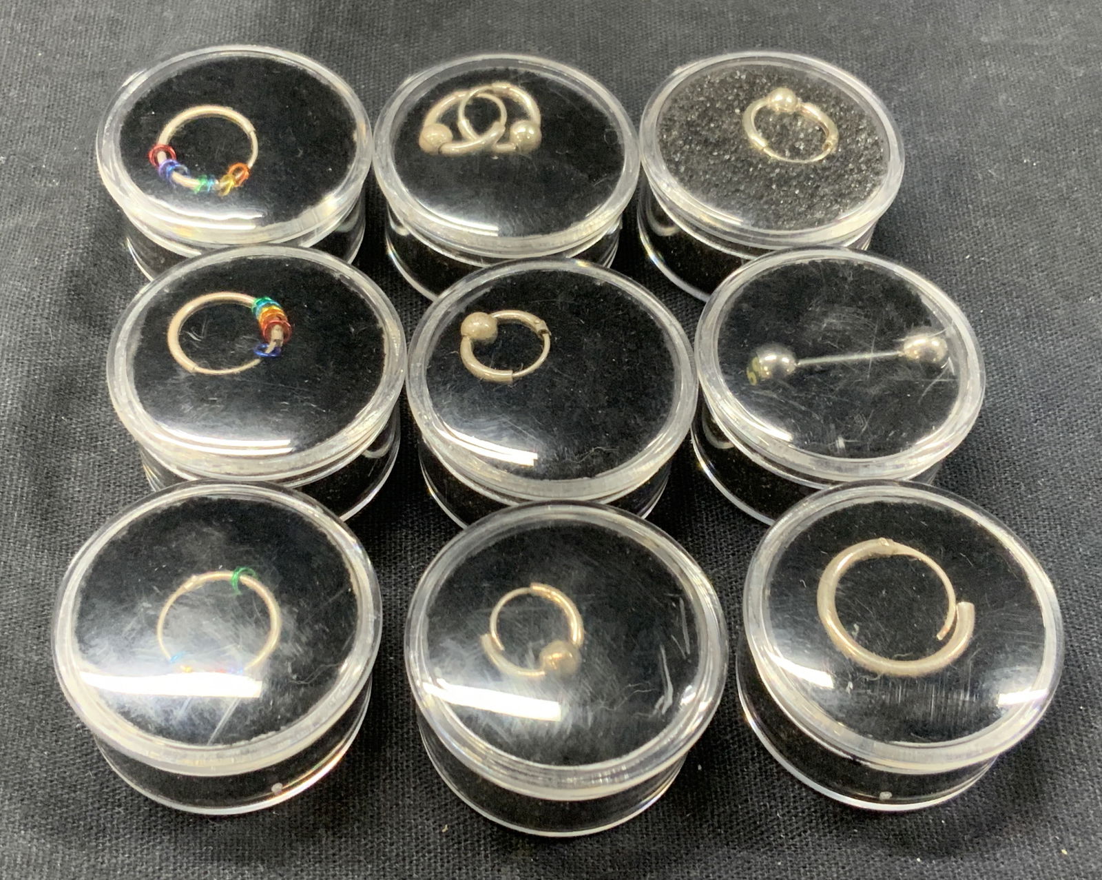 Lot 9 Sterling Silver Earrings & Body Jewelry: Lot of 9 pieces of jewelry. 3 sterling hoops with rainbow loops. Approx 9 mm wide. 2 pairs of hoops with single sphere in the center at 7mm wide. 1 hoop at 11 mm wide. And 1 sterling hoop at 8 mm wide