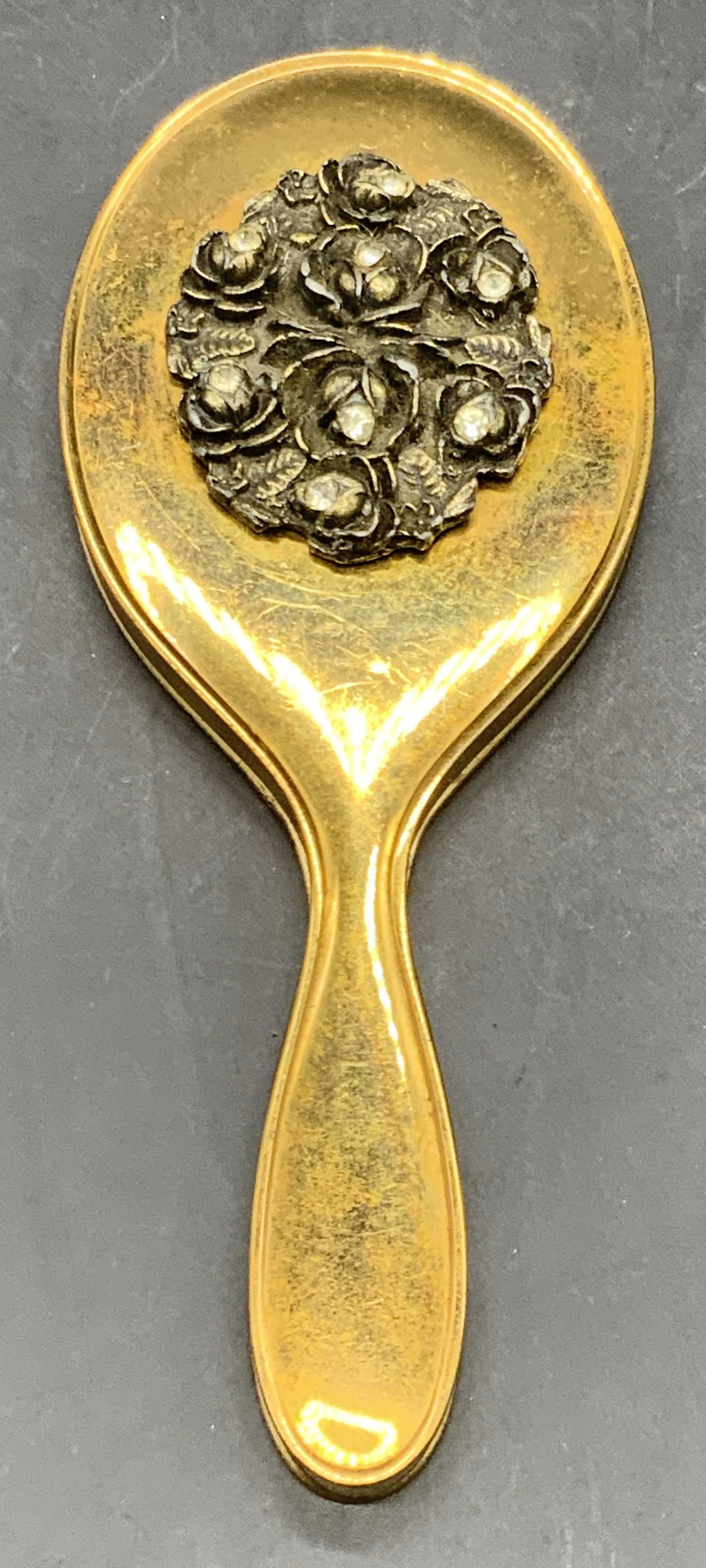 Vintage Brass Tone Metal Travel Hand Mirror: A vintage brass toned metal travel hand mirror / pocket hand mirror. Raised silver tone metal floral design to the reverse. Faceted colorless crystals to the florals. Measures approx. 5.25L x 2W in. D