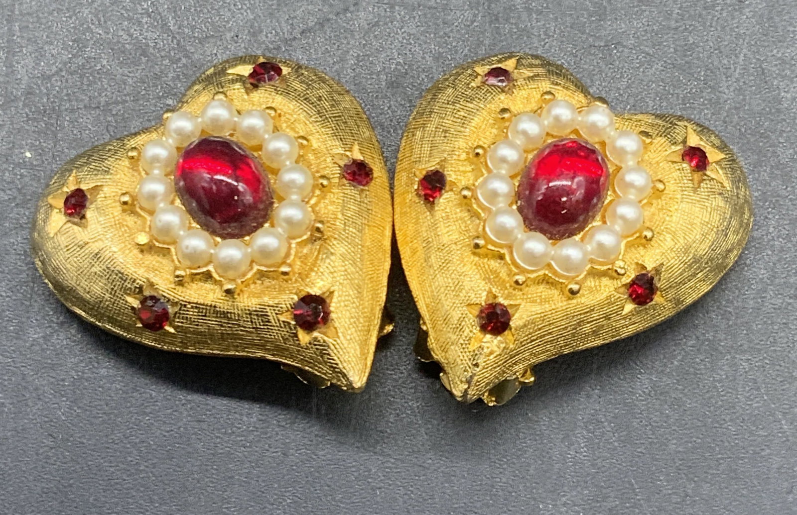Vintage Heart Form Crystal Clip On Earrings: Vintage gold tone metal heart form earrings featuring red crystals, pearlescent beads, and a red costume cabochon to the center. Reverse marked PAT PEND. Clip on backings. Measures approx. 1.25L x 1W 